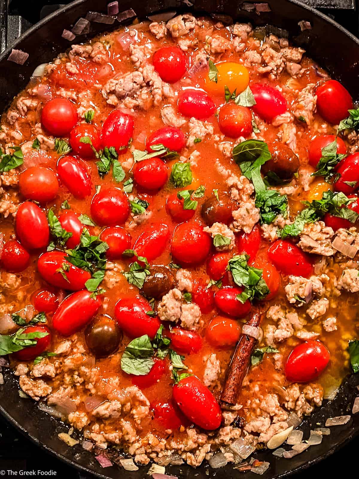 Cherry tomatoes, ground sausage and onions cooking in a skillet.