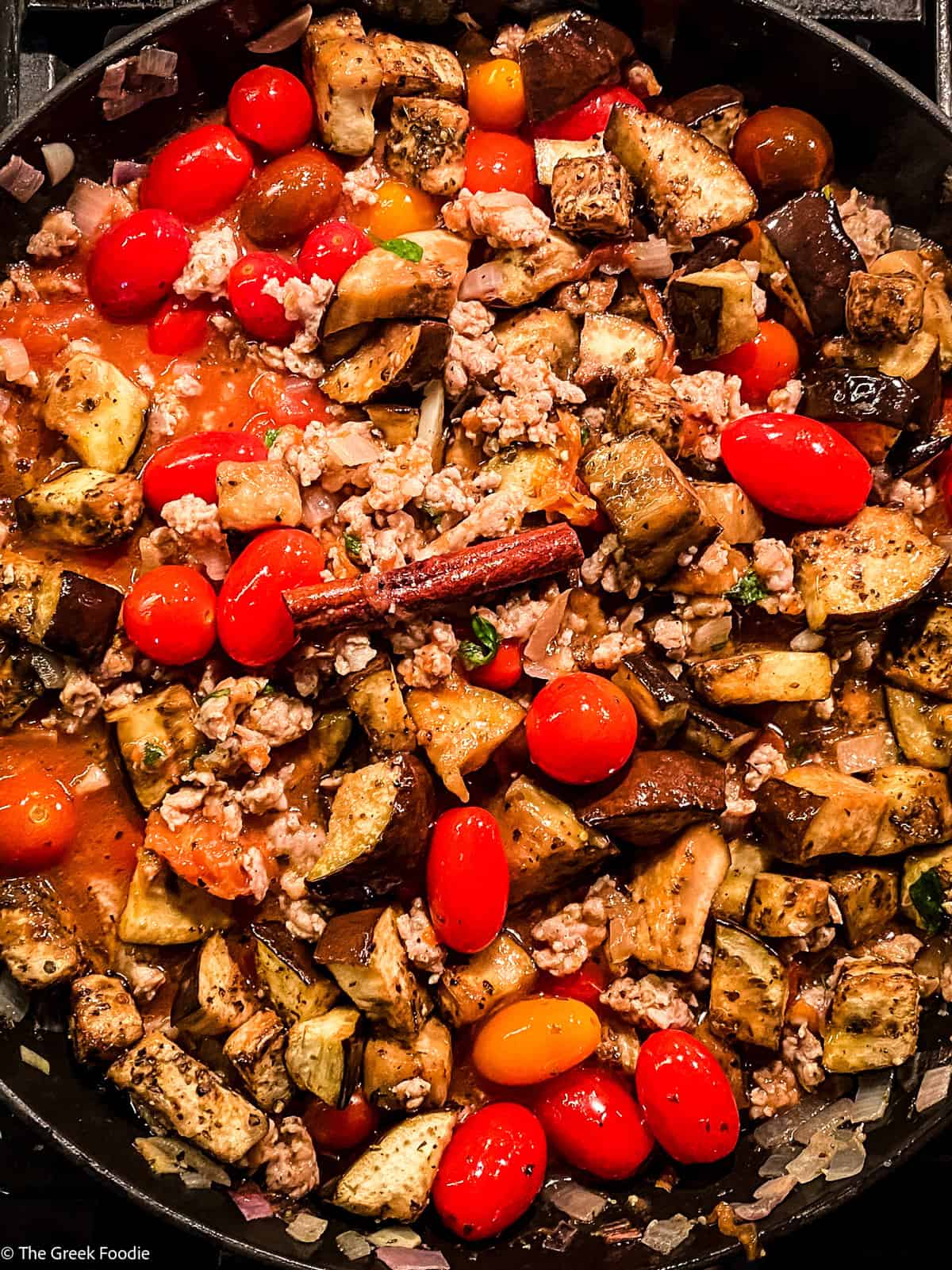 Cherry tomatoes, ground sausage and onions cooking in a skillet.