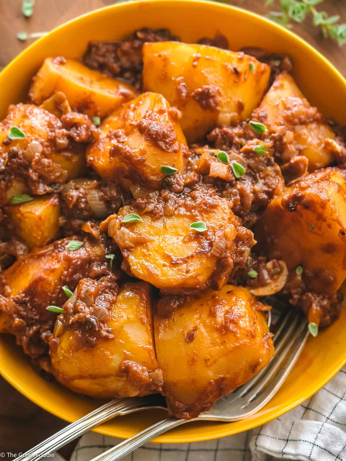 Patates yahni, Greek potato stew in red sauce, on a yellow plate.