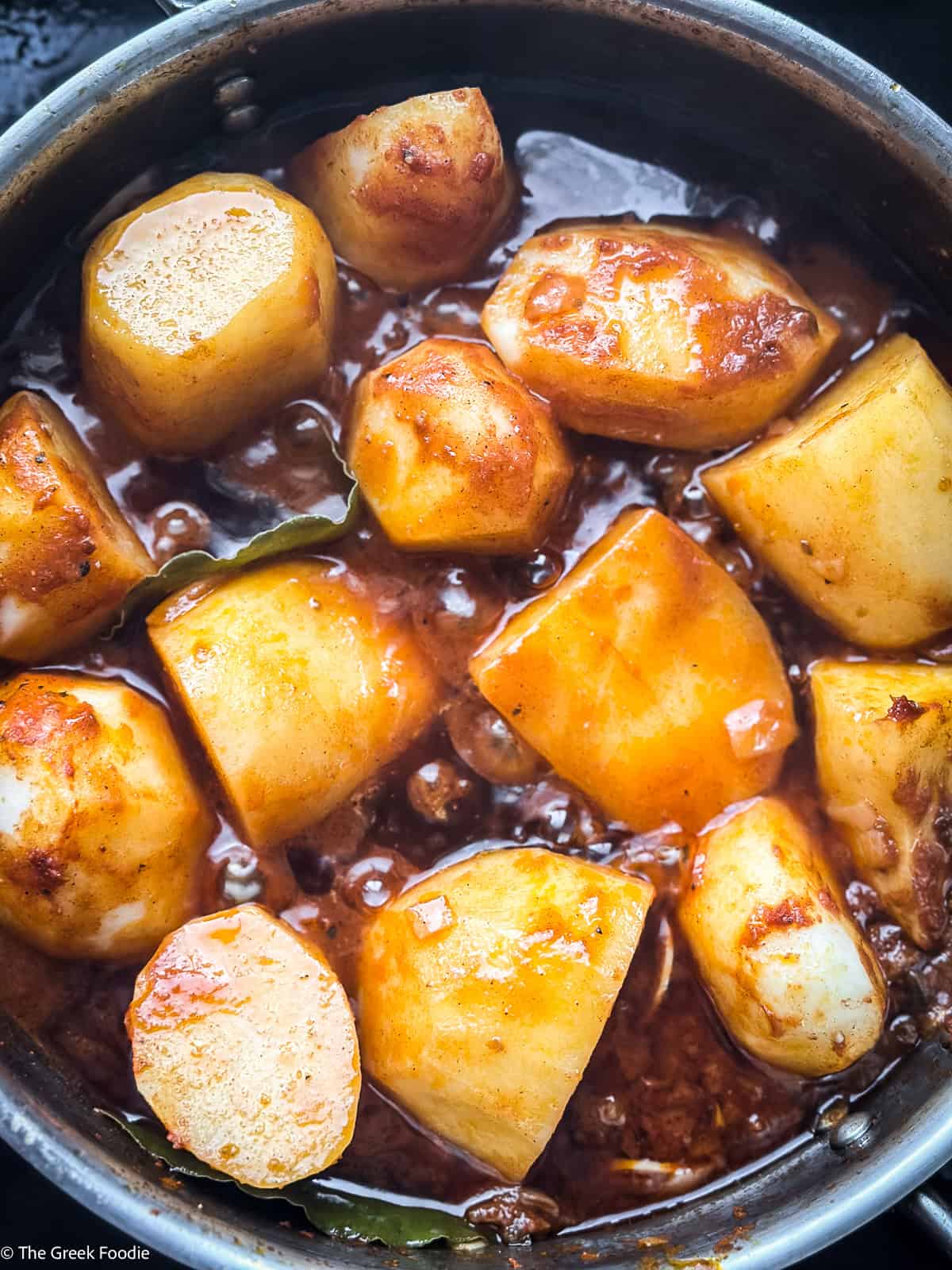A skillet cooking potatoes in red sauce.