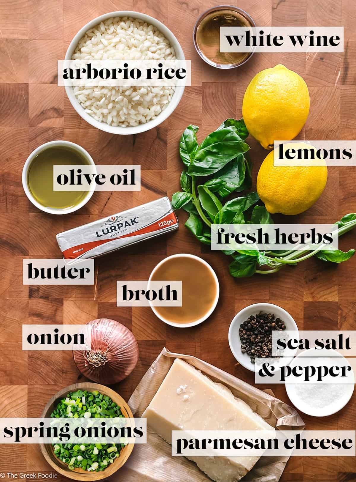 Bowls with arborio rice, broth, spring onions, salt and pepper, olive oil, two lemons, parmesan cheese, butter and fresh herbs.