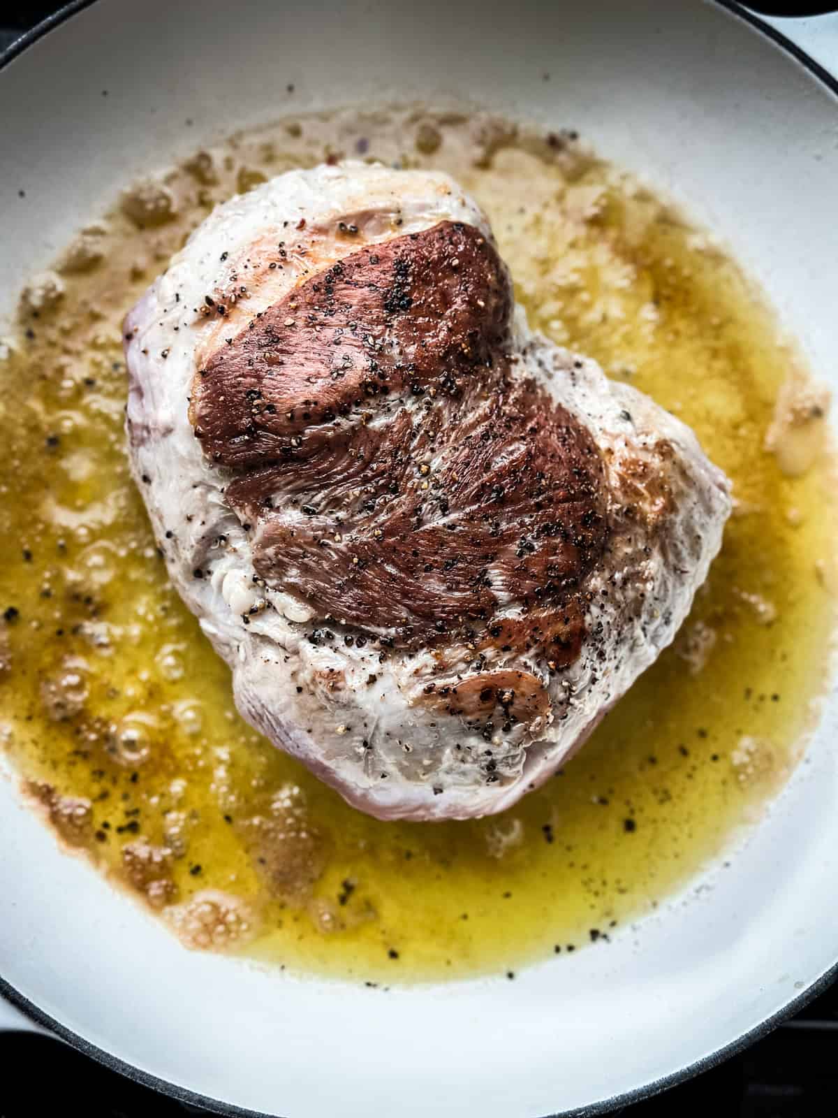 A pork shoulder in a skillet searing.