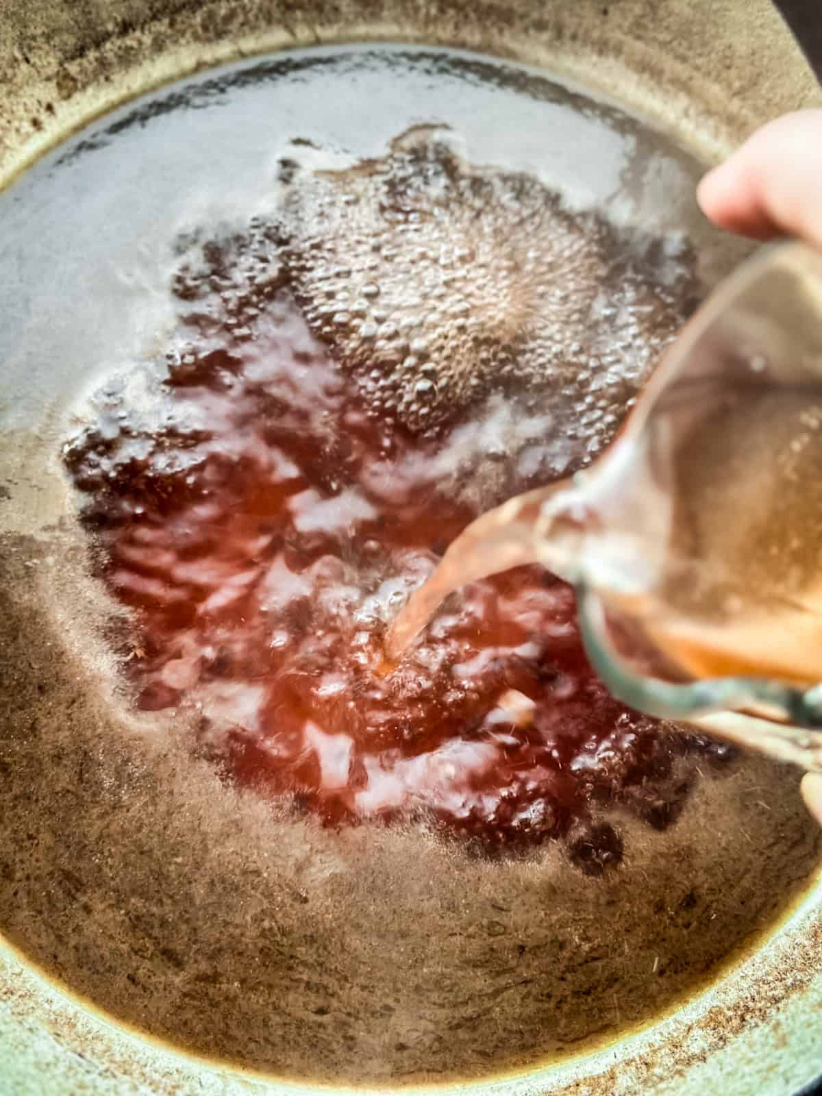 A pork shoulder in a skillet with wine sauce cooking.