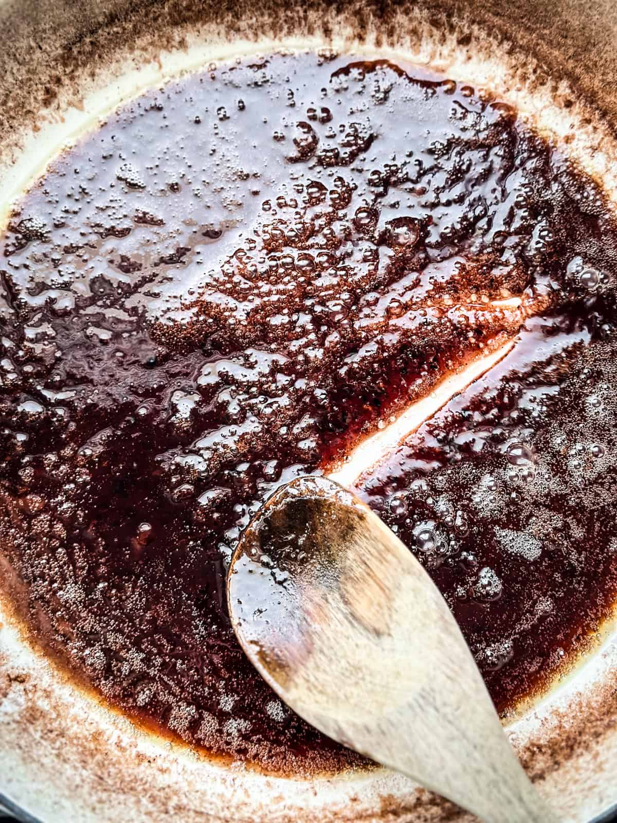 A wooden spoon stirring wine sauce in a skillet.