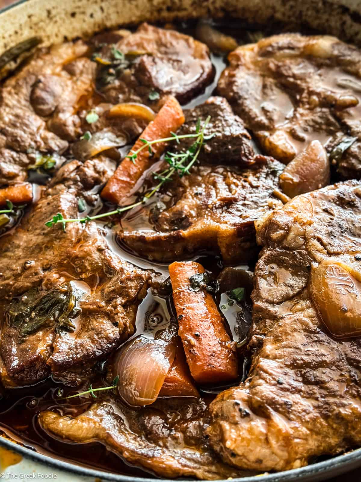 Close-up of sliced braised pork shoulder in a Dutch oven with carrots and celery in red wine sauce