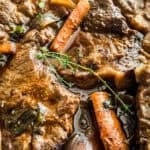 Sliced braised pork shoulder in a Dutch oven with carrots and celery in red wine sauce