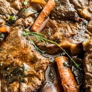Sliced braised pork shoulder in a Dutch oven with carrots and celery in red wine sauce