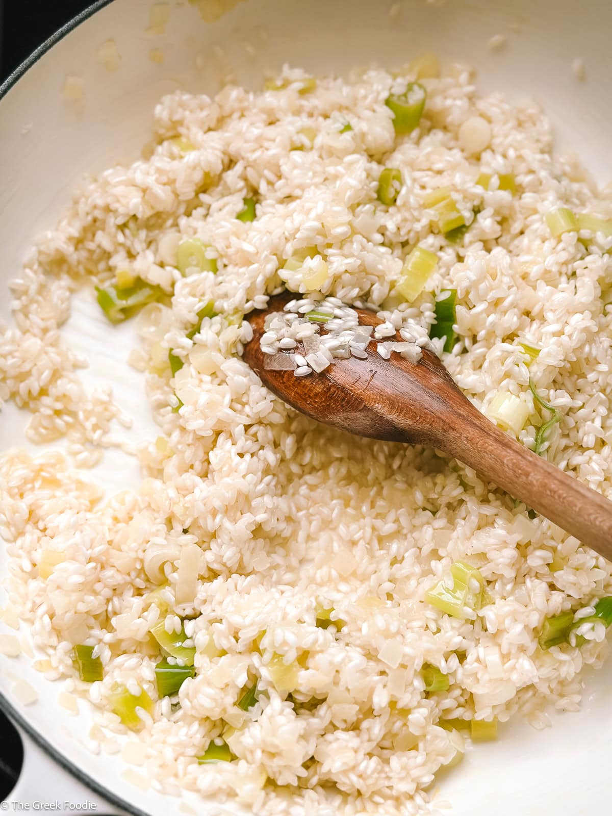 Arborio rice toasting with herbs and butter in a saucepan.