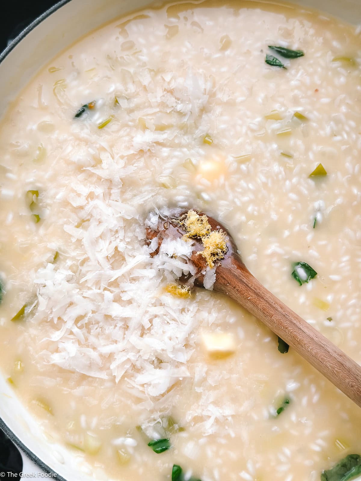 Risotto cooking in a sauce pan with a wooden spoon with butter, herbs, lemon zest and parmesan.