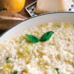 Creamy lemon herb risotto and a spoon in a white large saucepan, a lemon, parmesan at the back.