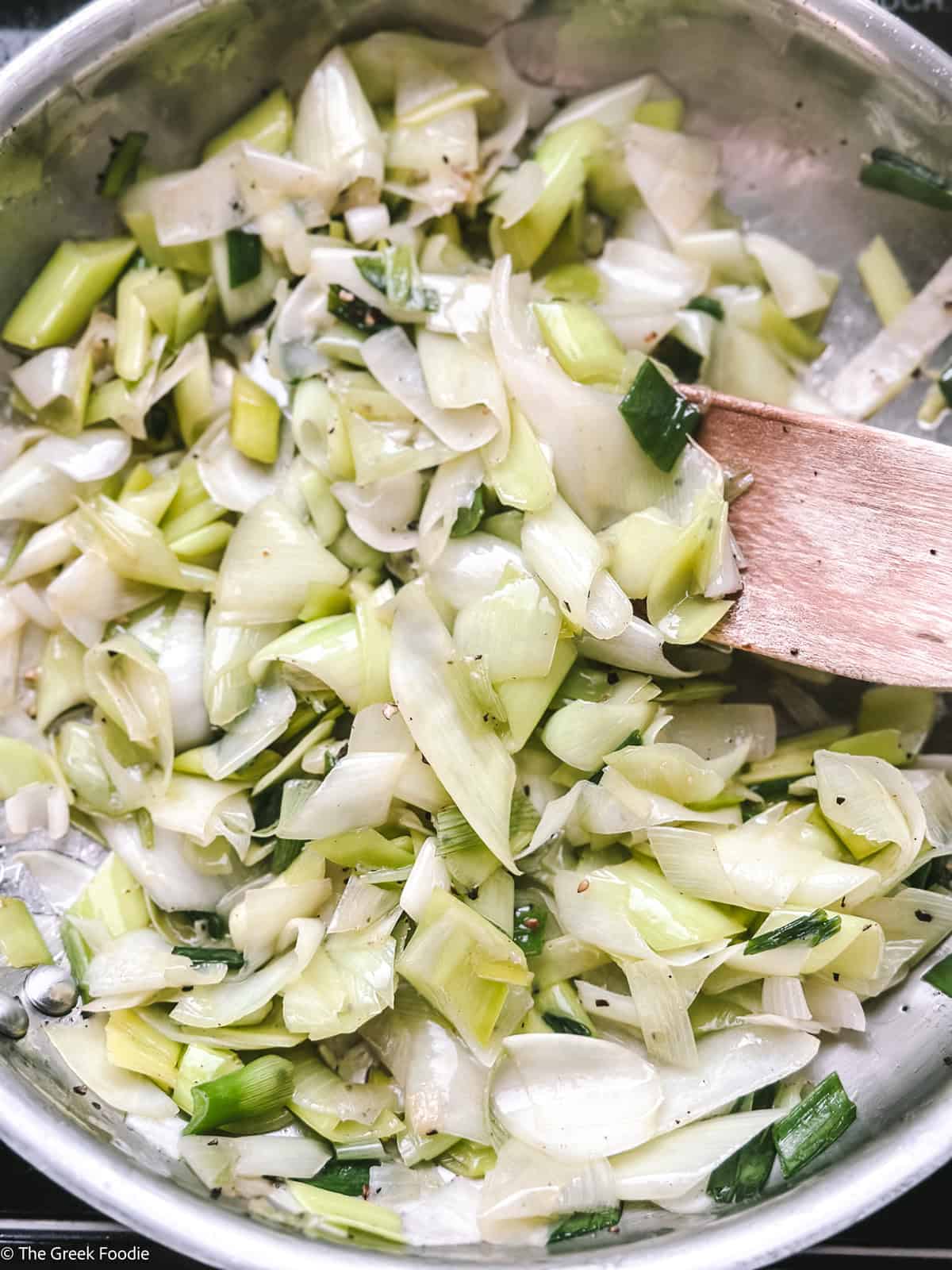 Leeks and onions cooking with a wooden spoon.