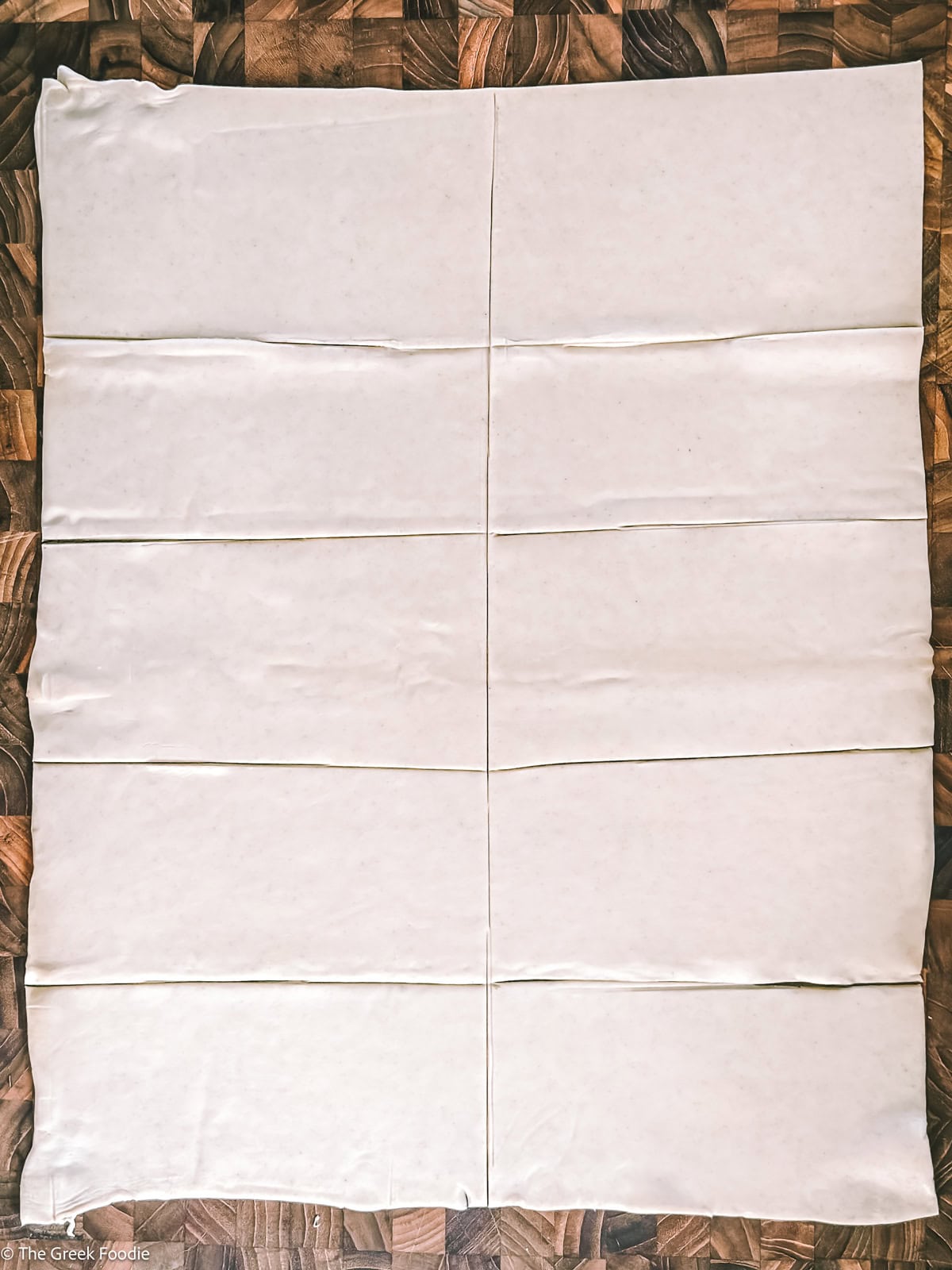 A puff pastry sheet on a wooden board cut into ten pieces.