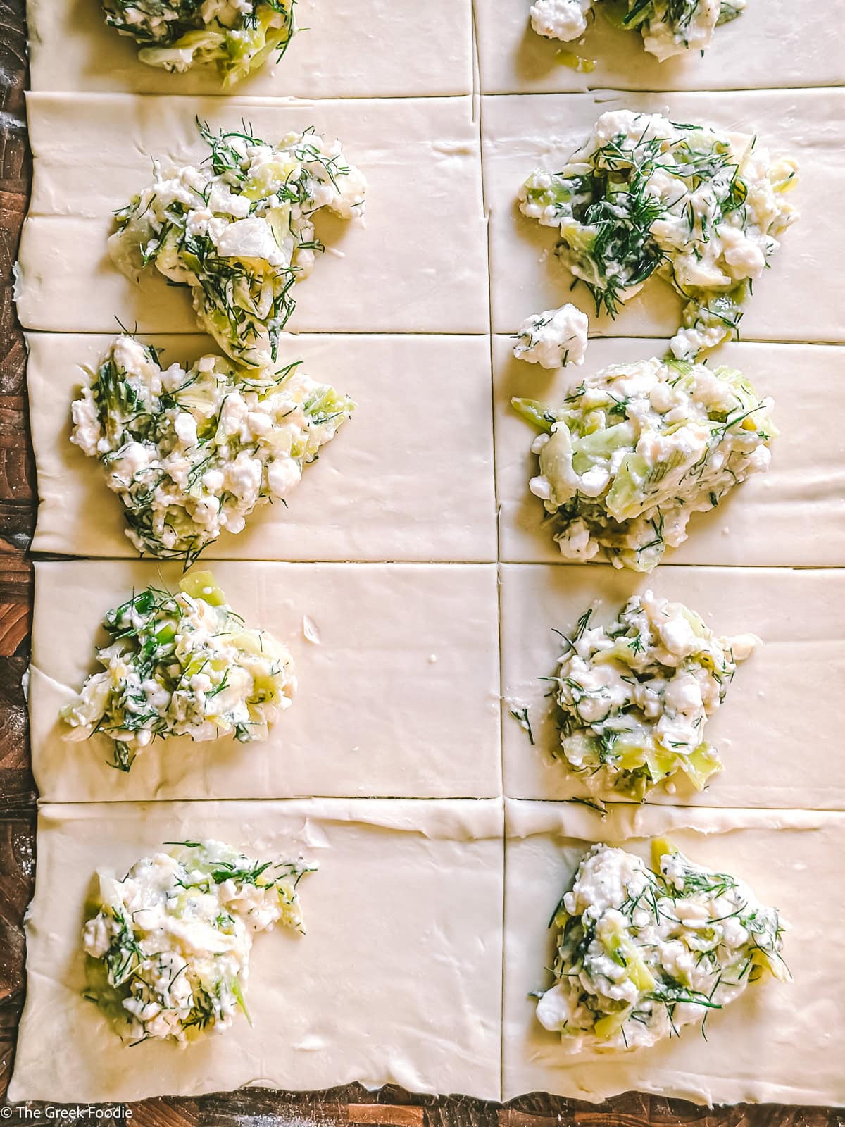 Puff pastry strips with feta cheese filling on them, on a wooden board.