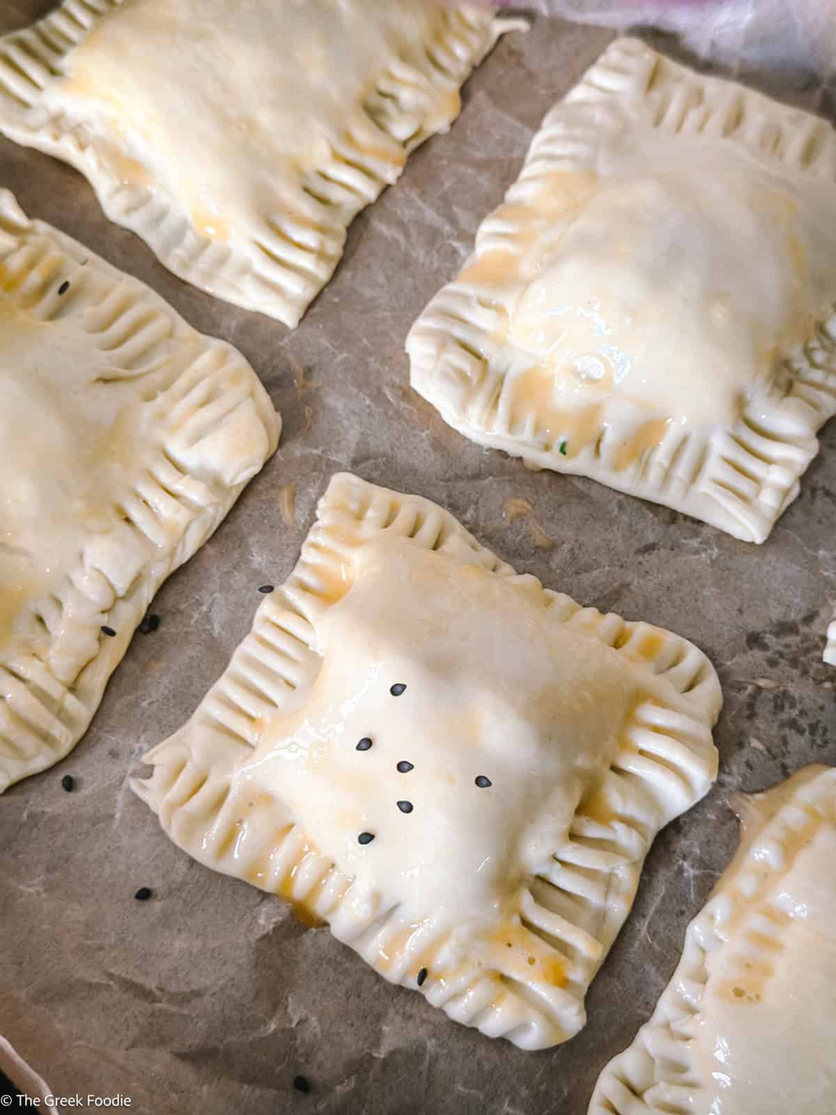 Cheese puff pastries with egg wash and sesame seeds o parchment paper.