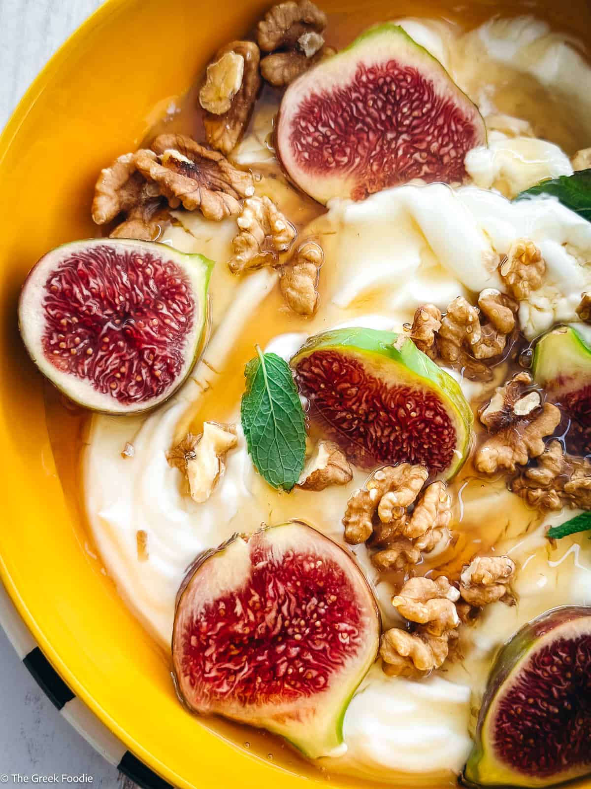 A plate with yogurt, sliced figs, walnuts and honey and a spoon.