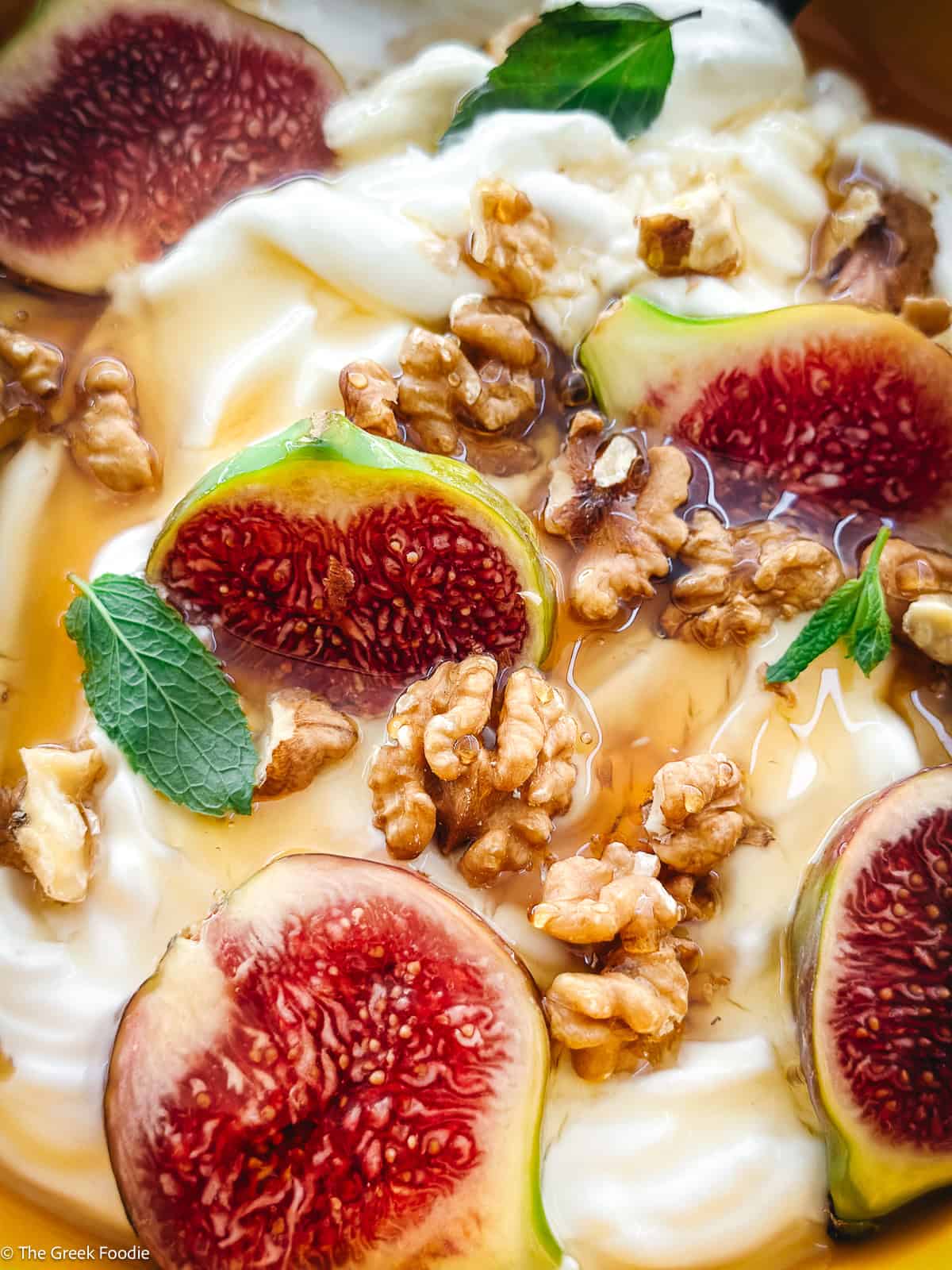 A plate with yogurt, sliced figs, walnuts and honey and a spoon.