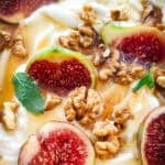 A plate with yogurt, sliced figs, walnuts and honey and a spoon.