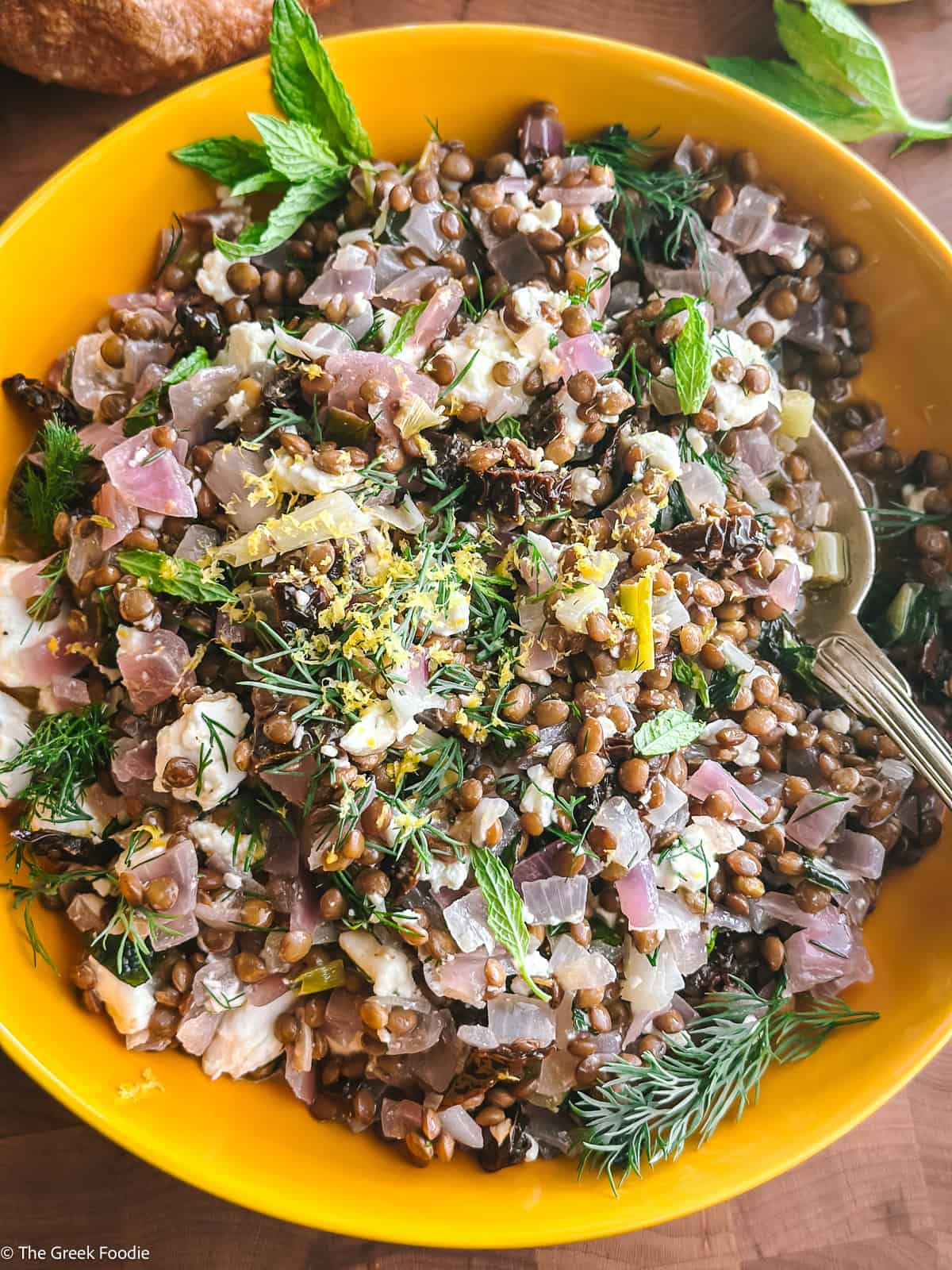 Greek lentil salad with feta in a bowl with a spoon, on a table.