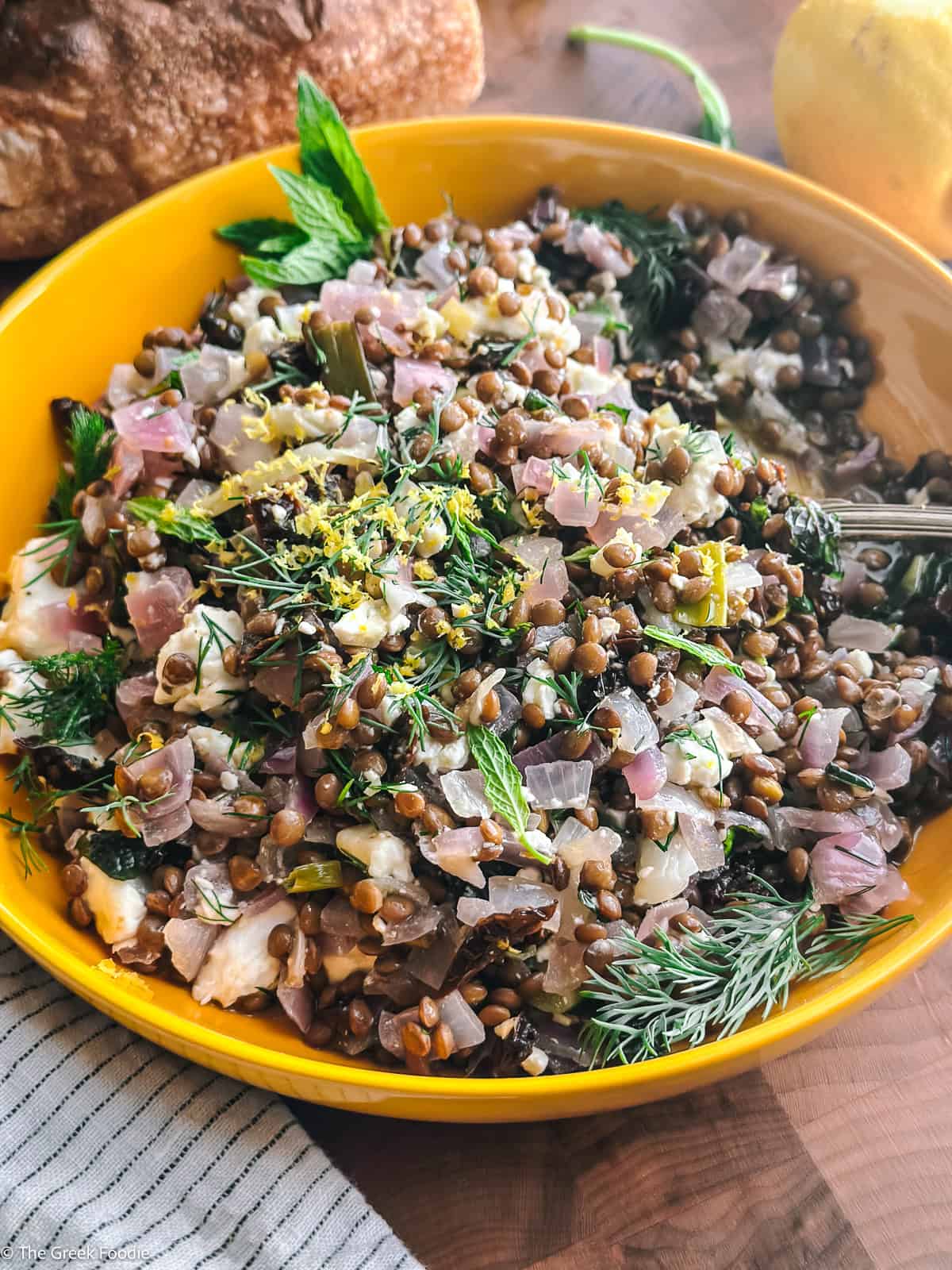 Greek lentil salad with feta in a bowl with a spoon, on a table.