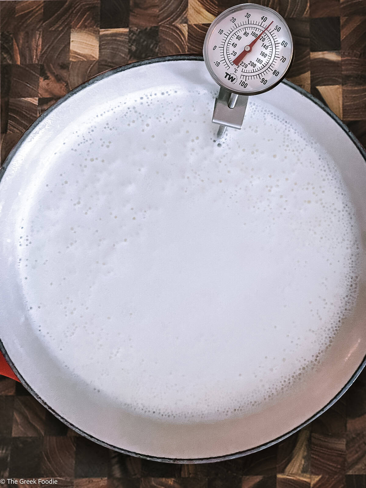 A big sauce pan with milk and a thermometer.