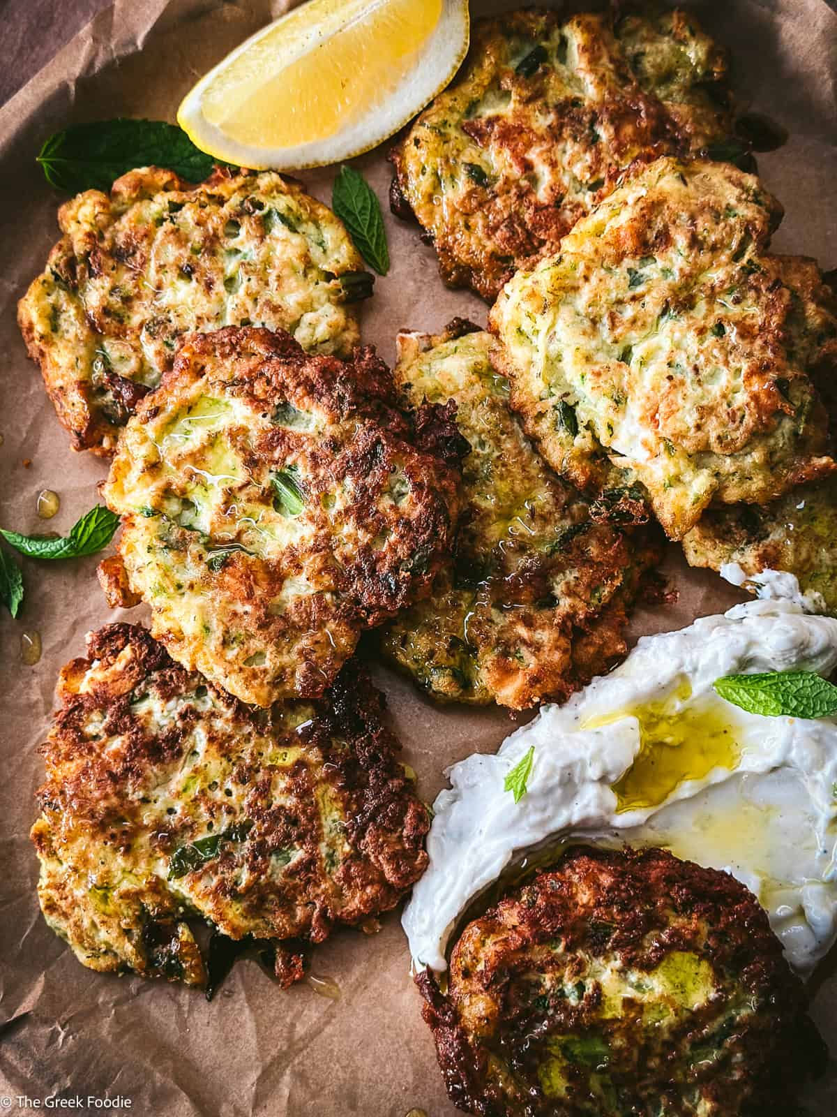 Zucchini fritters on parchment paper with some yogurt and herbs.