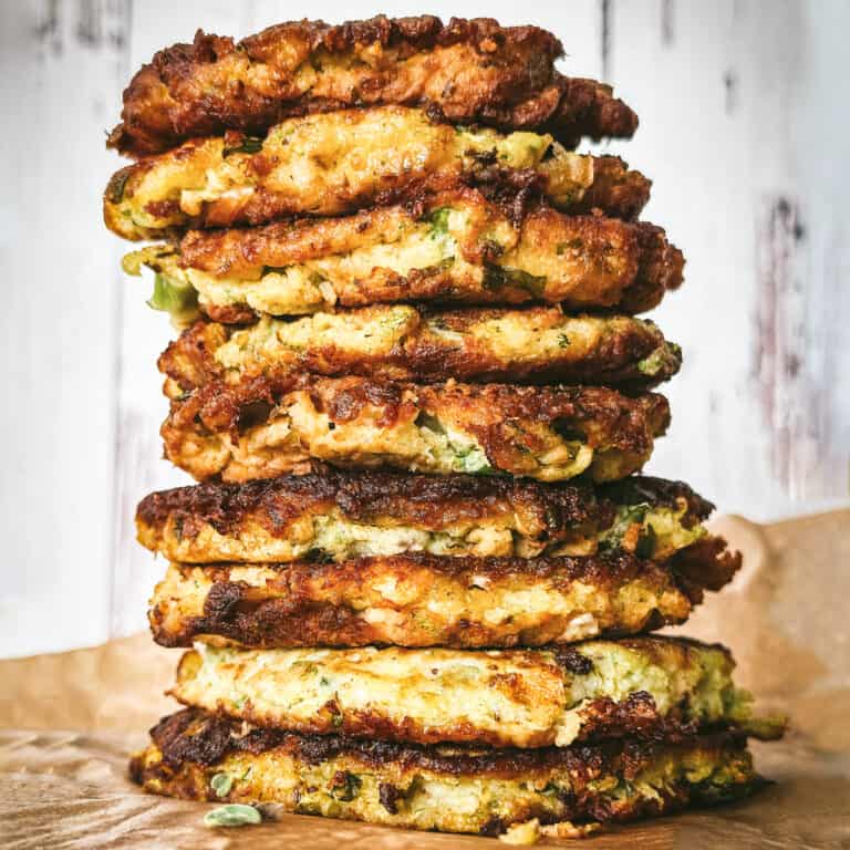 Stacked zucchini fritters kolokithokeftedes on a table with herbs.