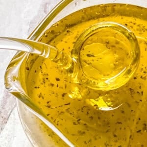 A sause jar with a glass spoon and ladolemono, olive oil and lemon sauce.