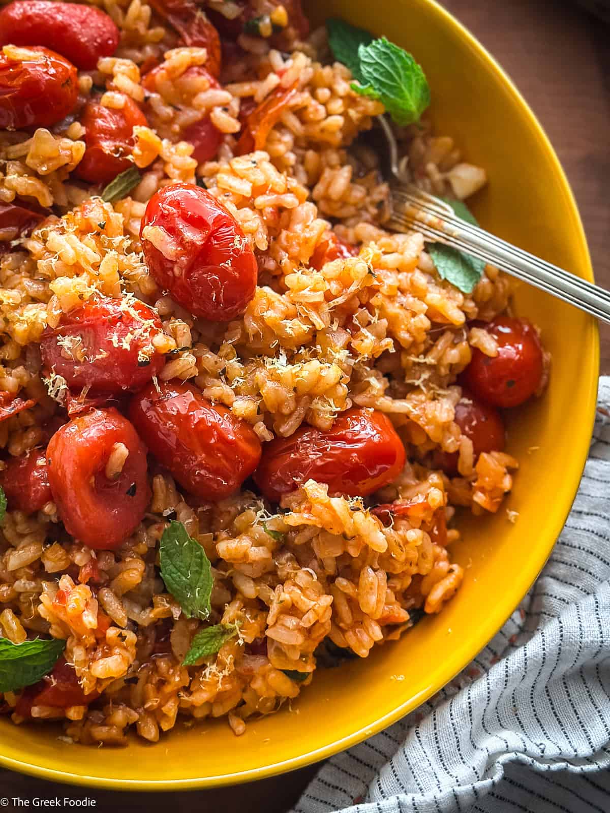 A yellow plate with tomato rice-ntomatorizo, herbs and a spoon.