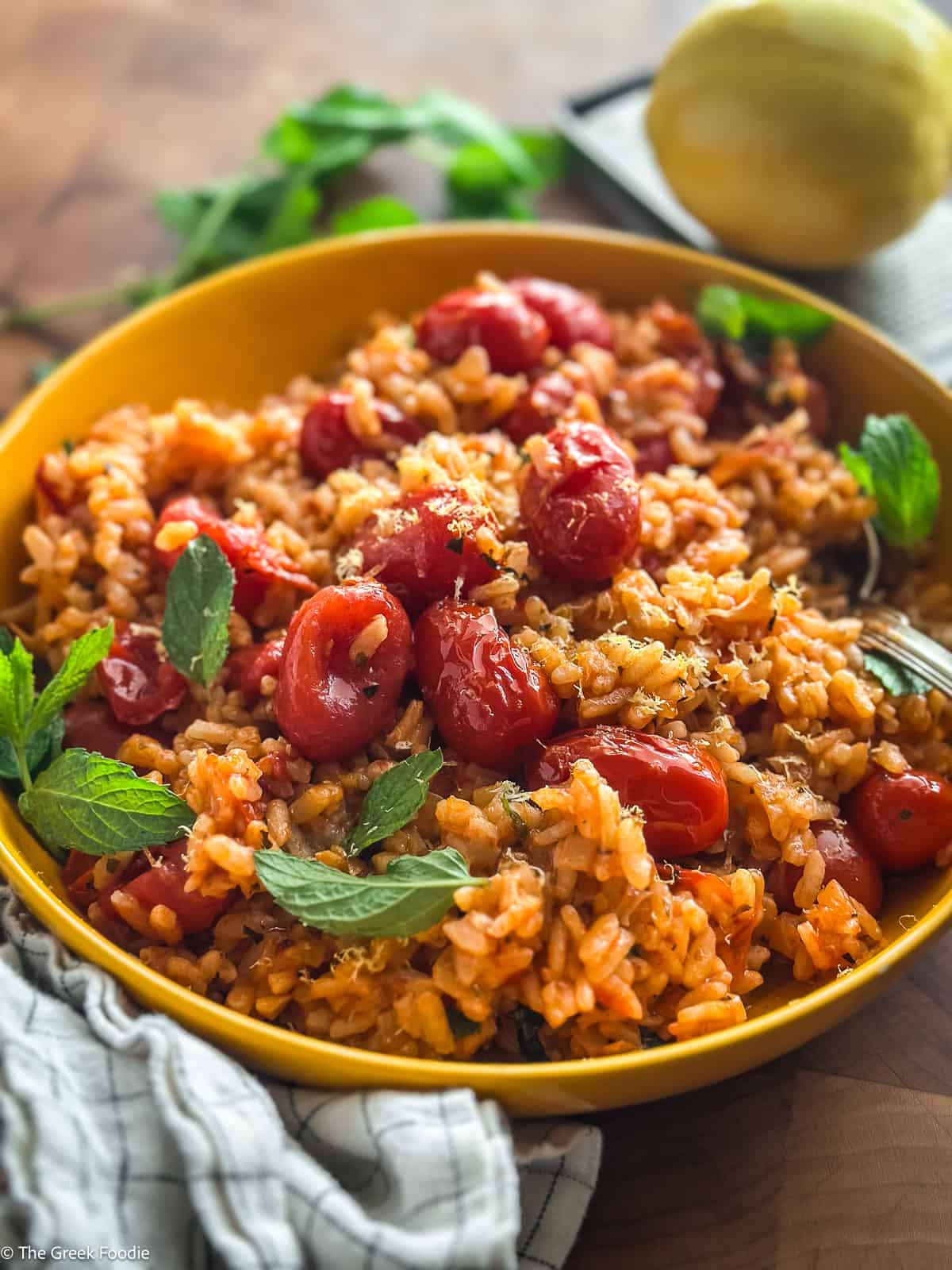 A yellow plate with tomato rice-ntomatorizo, herbs and a spoon.
