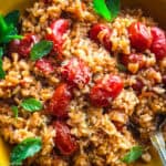 A yellow plate with tomato rice-ntomatorizo, herbs and a spoon.