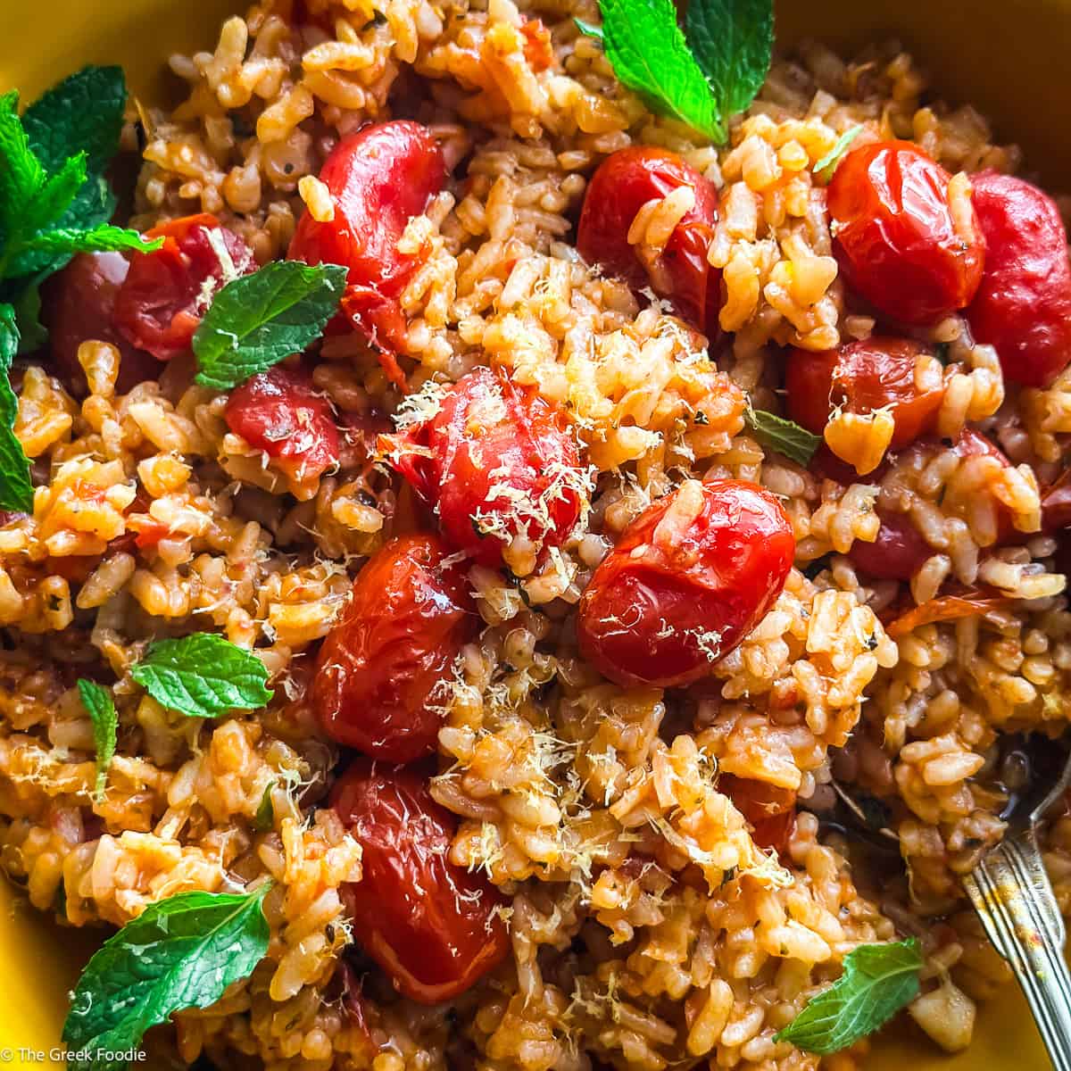 A yellow plate with tomato rice-ntomatorizo, herbs and a spoon.