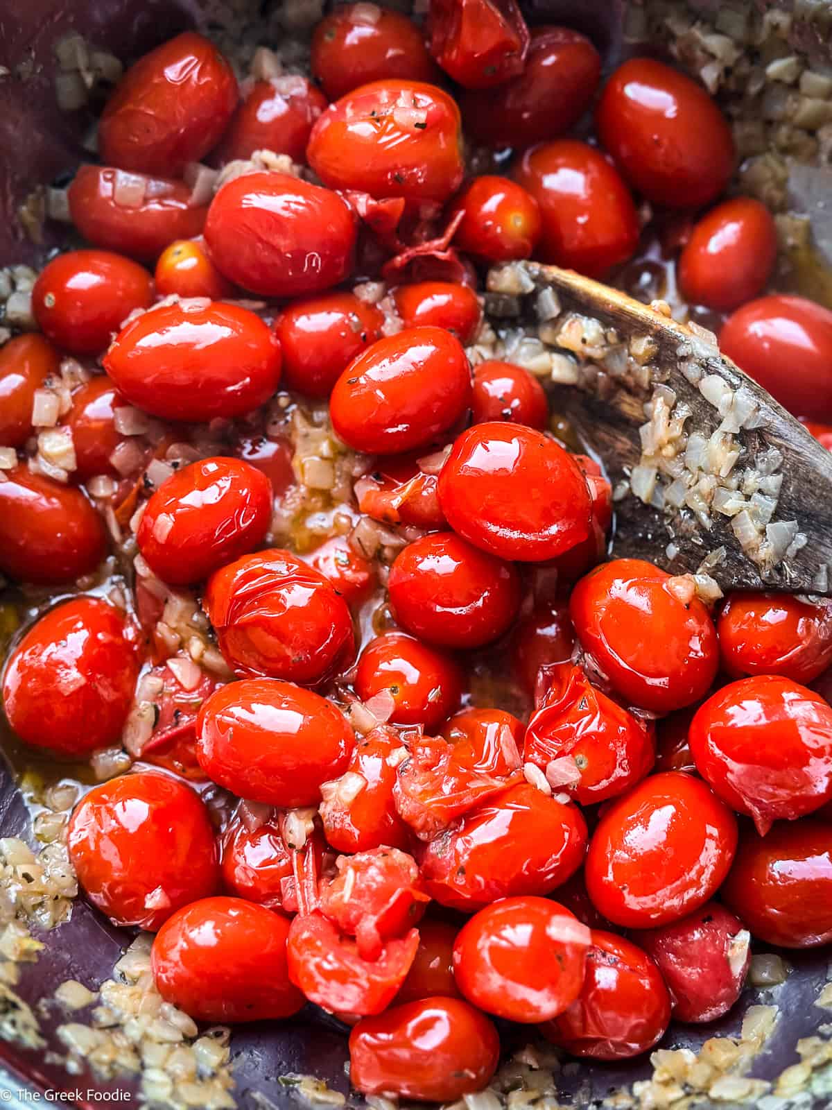 Cherry tomatoes with diced onion cooking and a wooden fork.