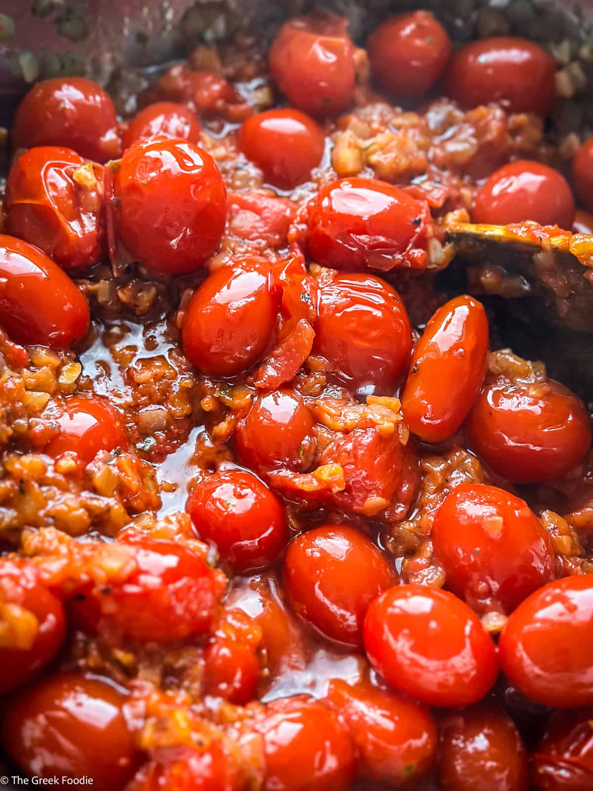 Cherry tomatoes with diced onion and tomato paste cooking and a wooden fork.