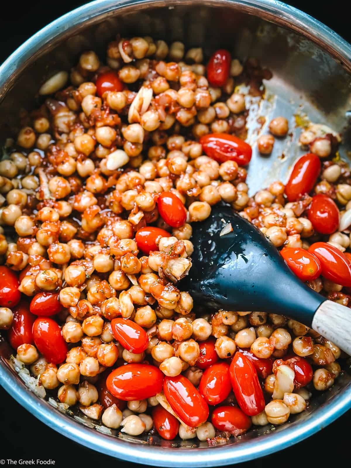 Chickpeas and tomatoes with a wooden spoon in a sauce pan.