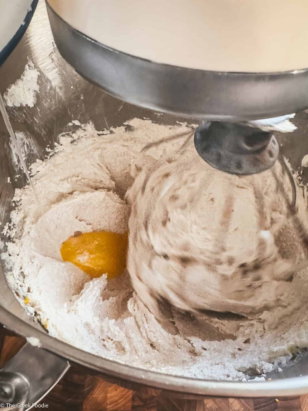 A whisk beating cake batter and eggs in a mixer.