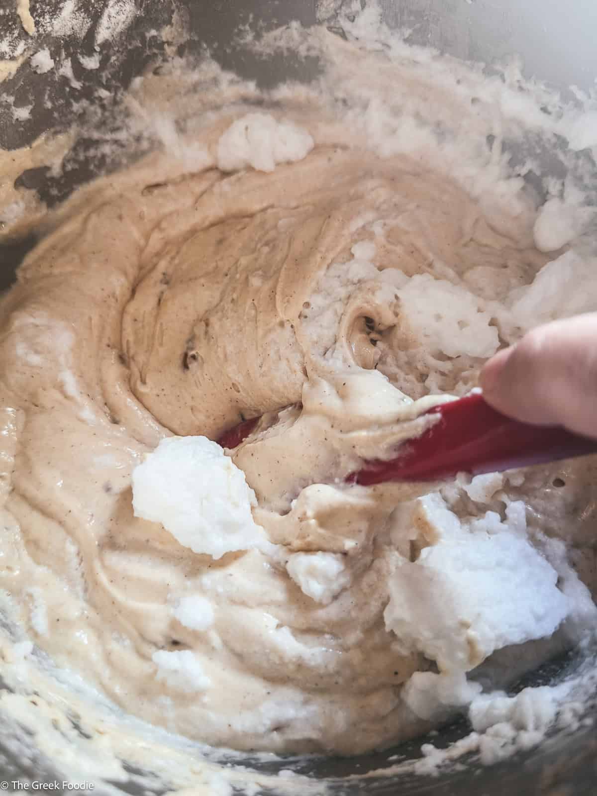 A hand holding a spatula folding egg whites into batter.