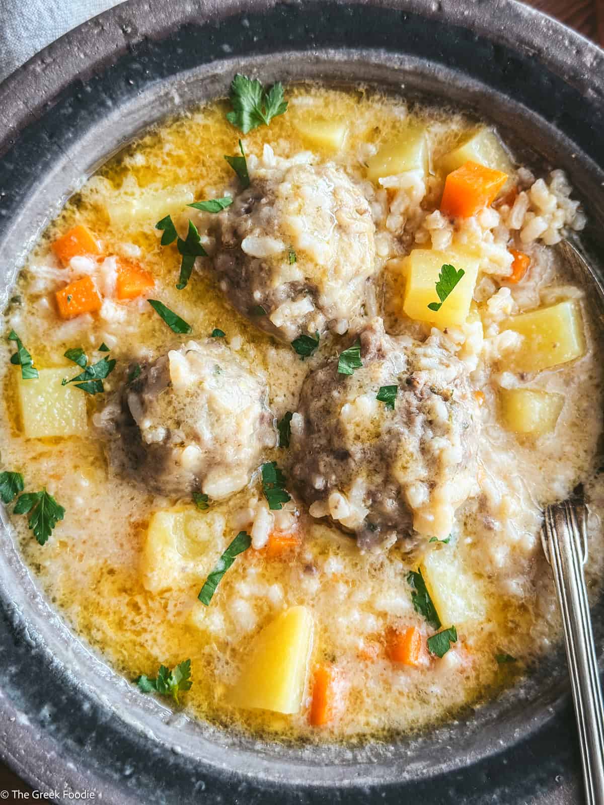 Youvarlakia meatballs with rice, broth in a plate with a spoon.