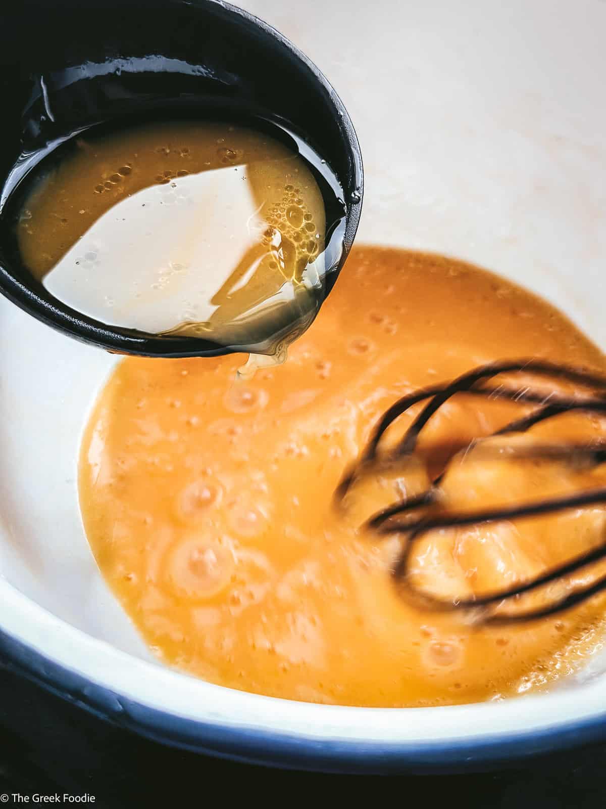 Broth poured in egg and lemon and a whisk whisking.