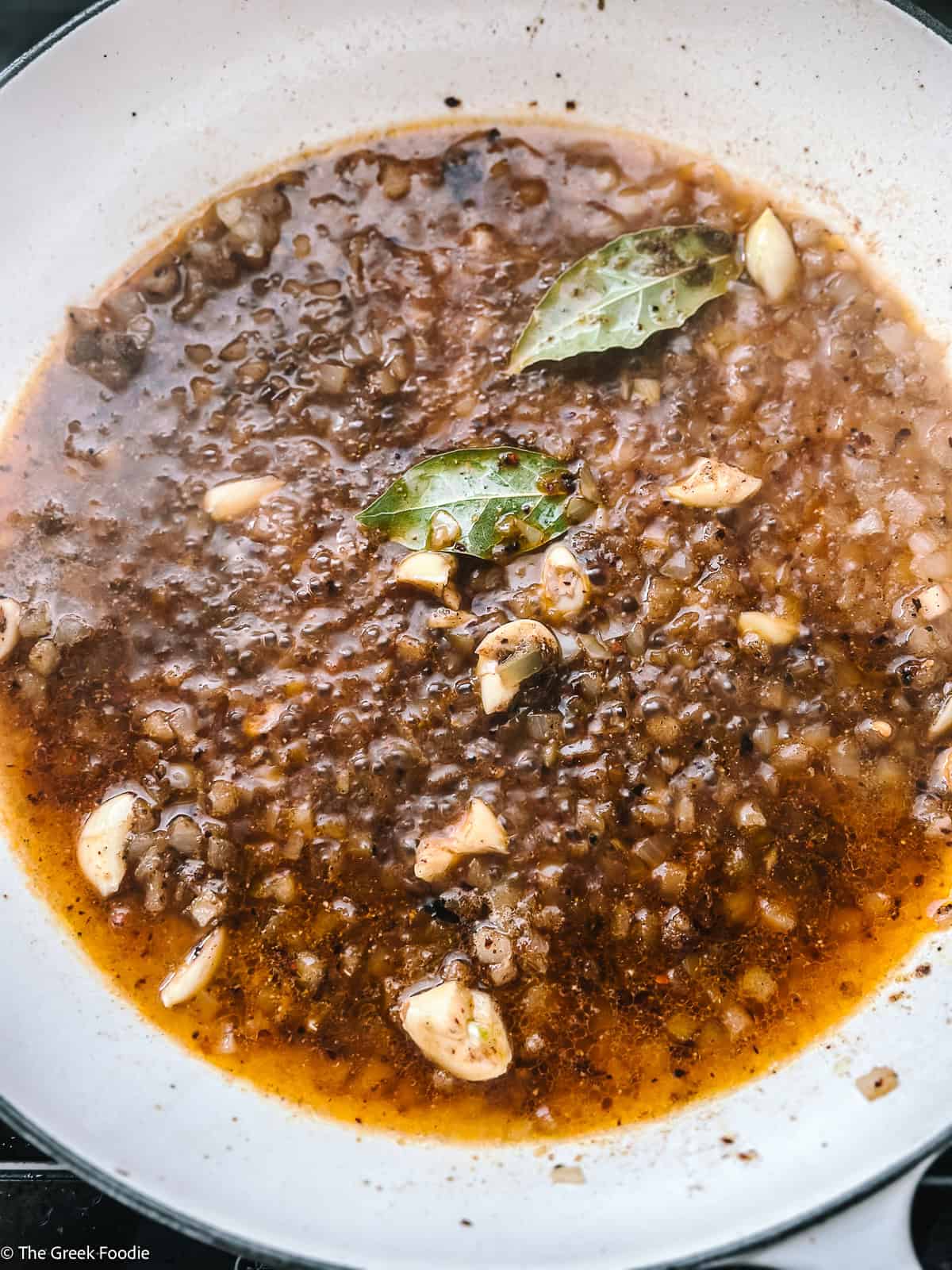 Broth with onion, bay leaves and seasonings cooking in a white pot.