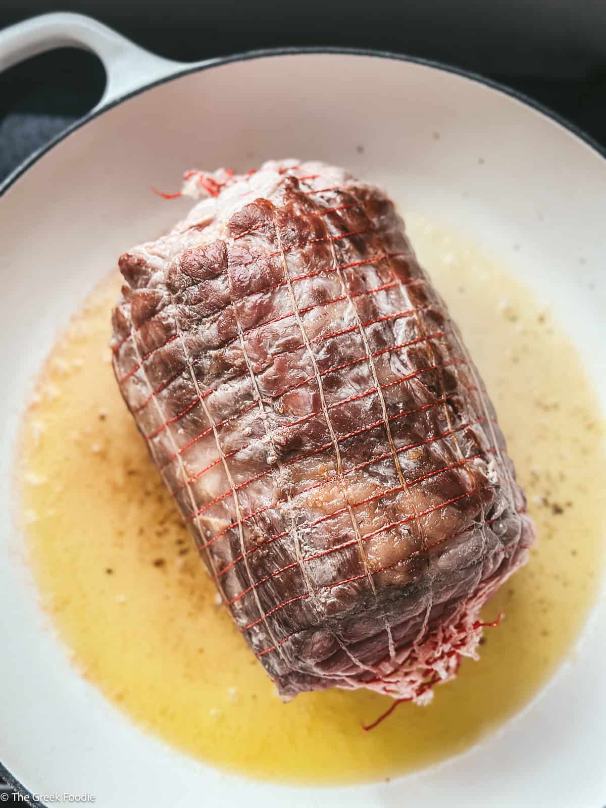 A pork shoulder wrapped in a net, searing in a dutch oven pot.