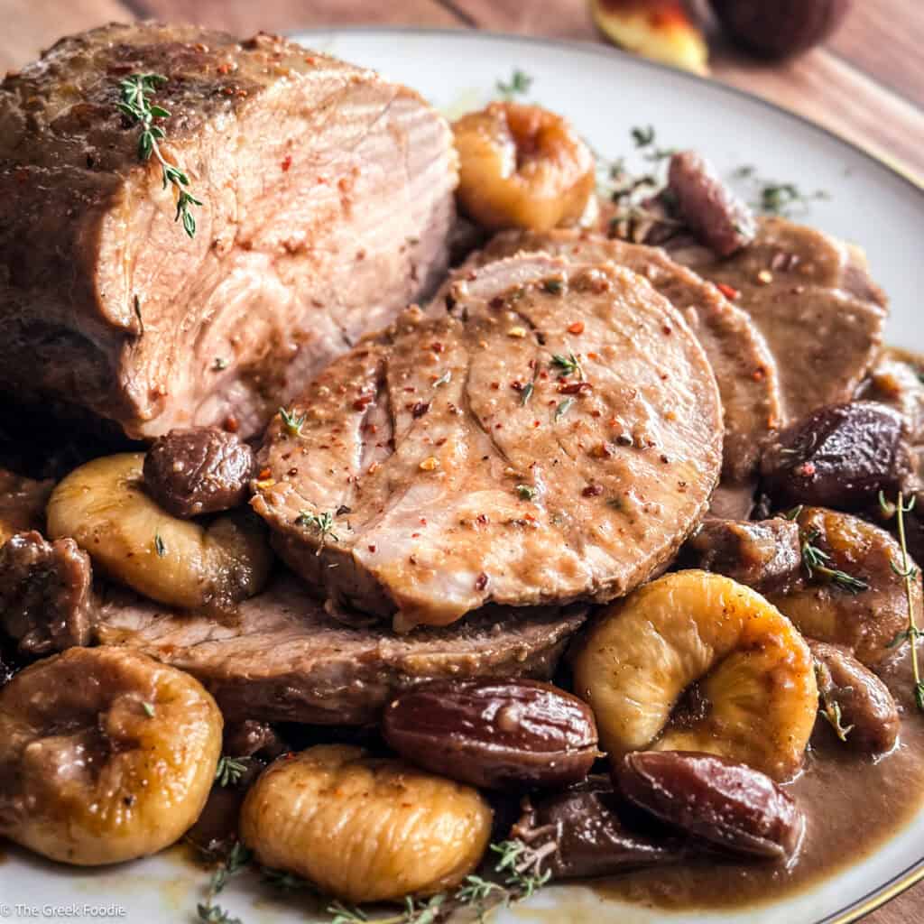 A plate with slices of pork pot roast with dried fruit, on a table.