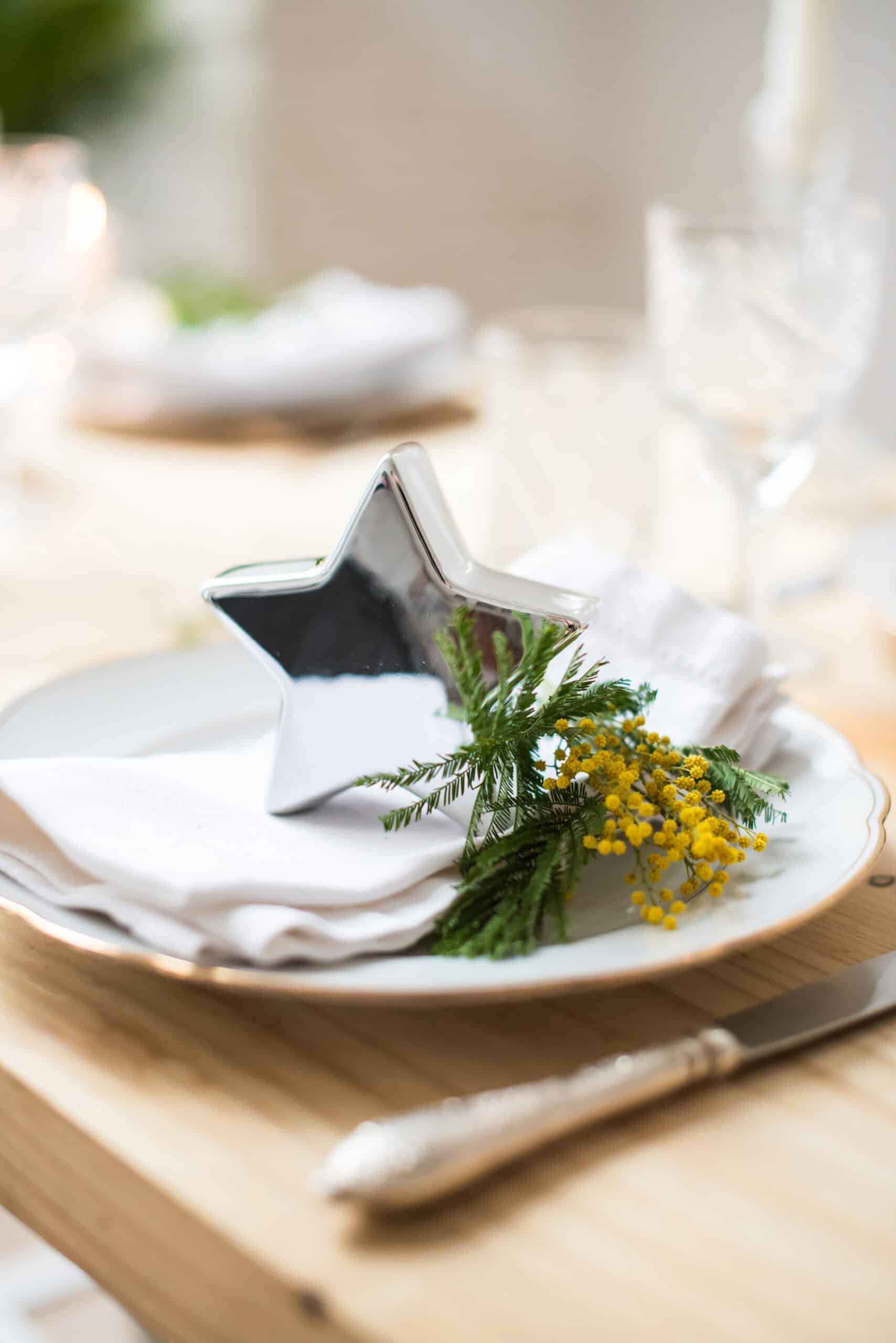 A silver star box with flowers on a plate setting on a dinner table
