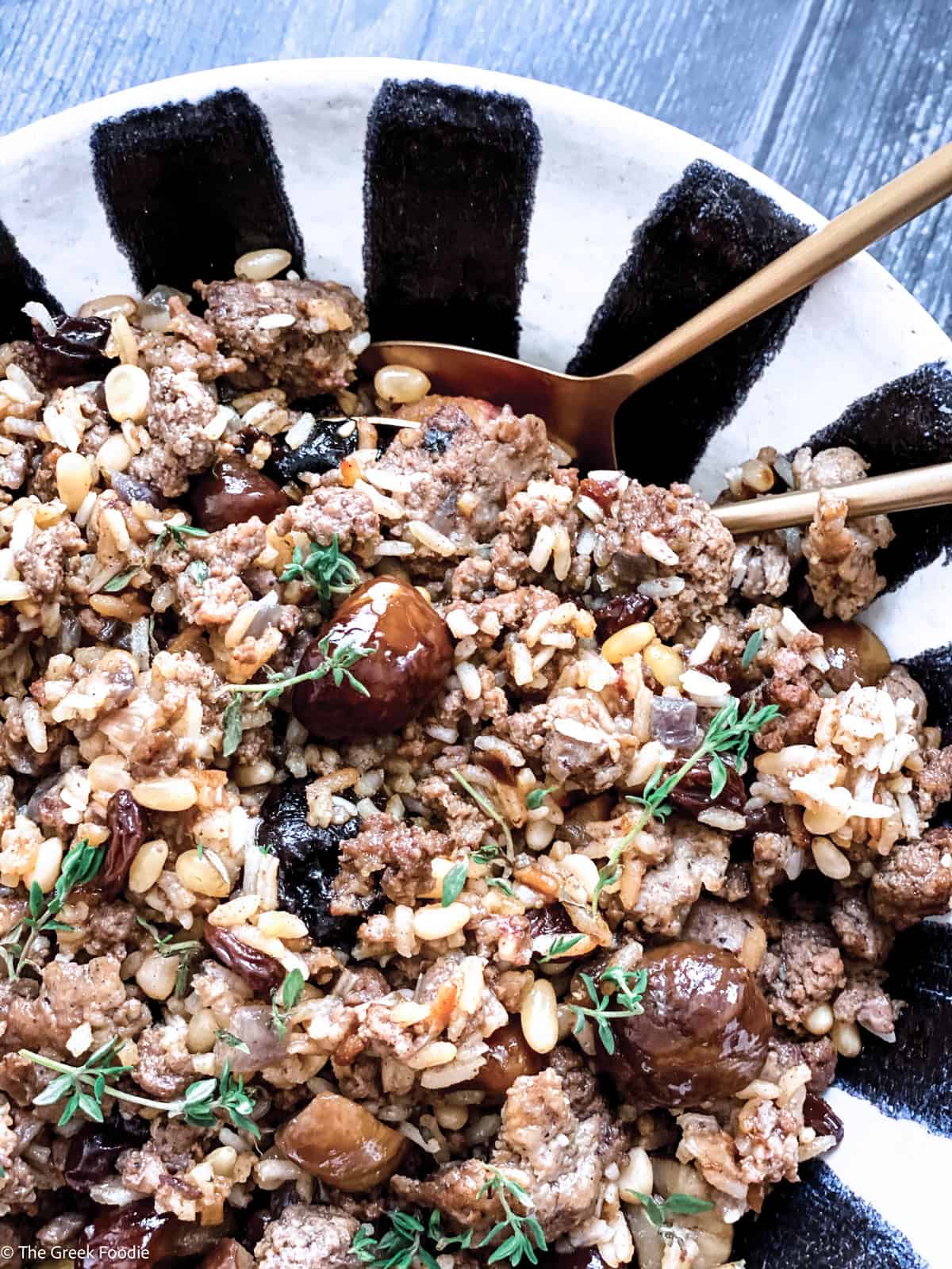 A bowl with Greek turkey stuffing on a table with a serving spoon.