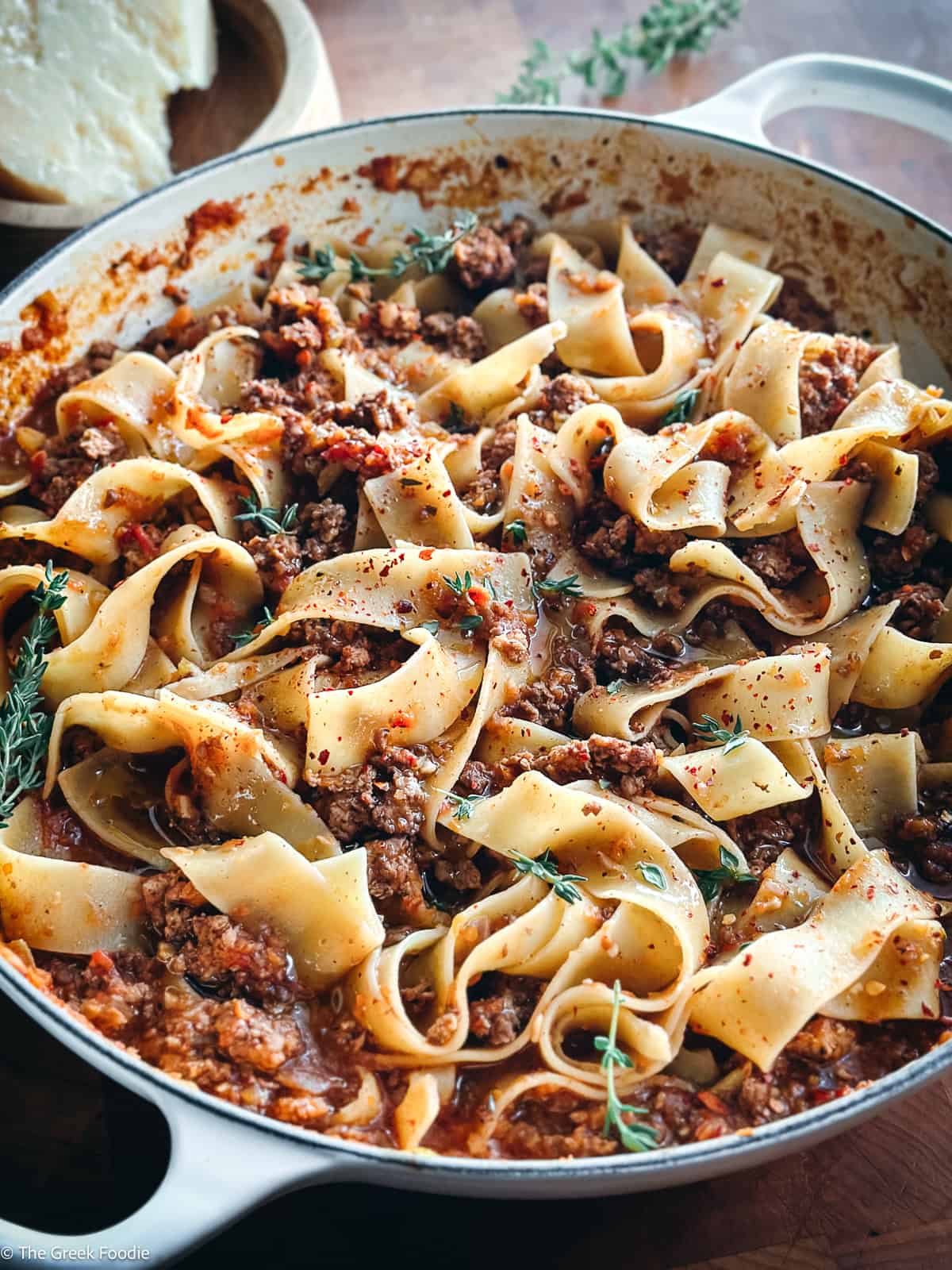 A white dutch oven with chicken bolognese with papardele pasta and two serving utensils on a table.