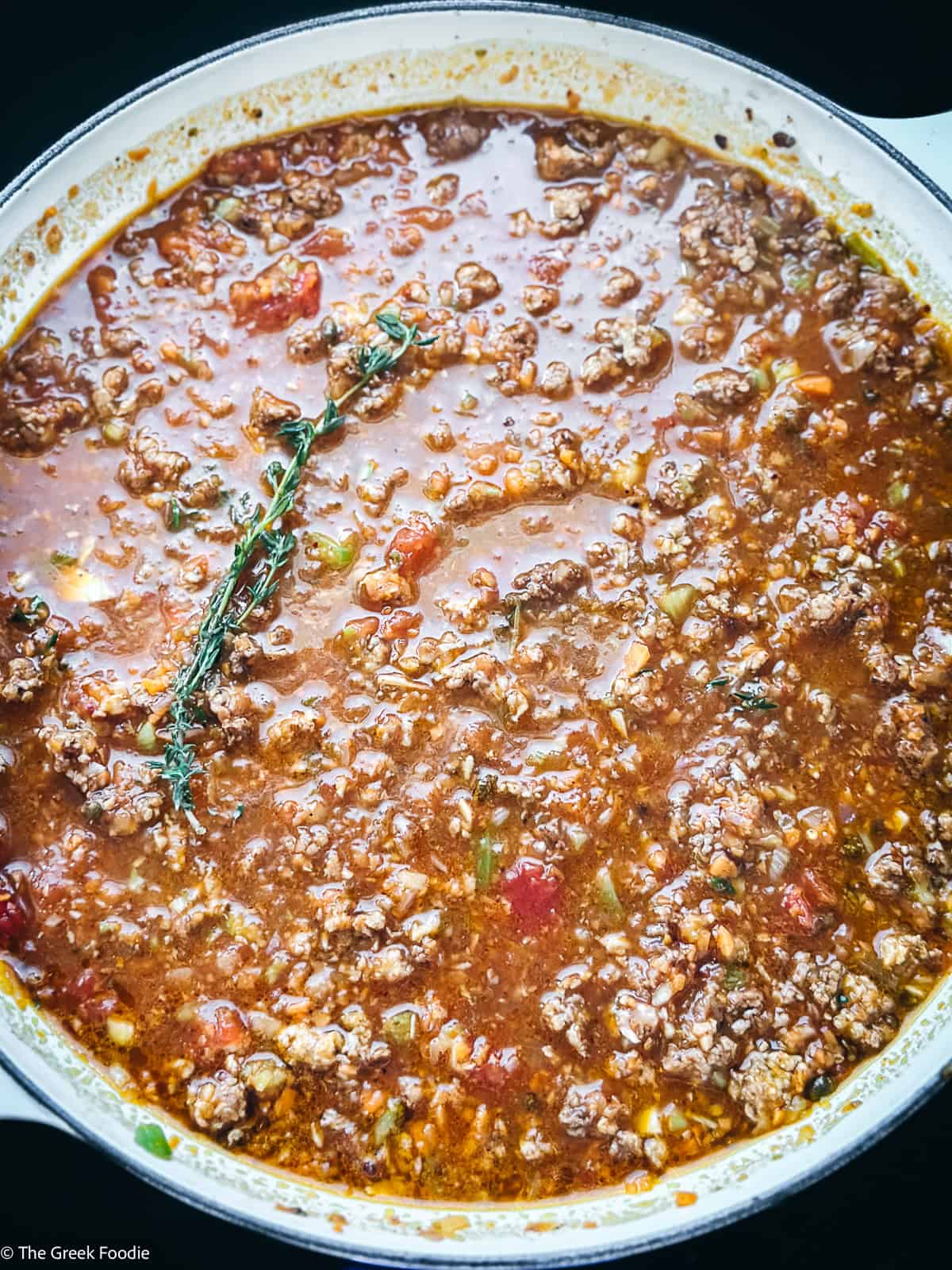 Chicken bolognese in a pot cooking with a sprig of thyme.