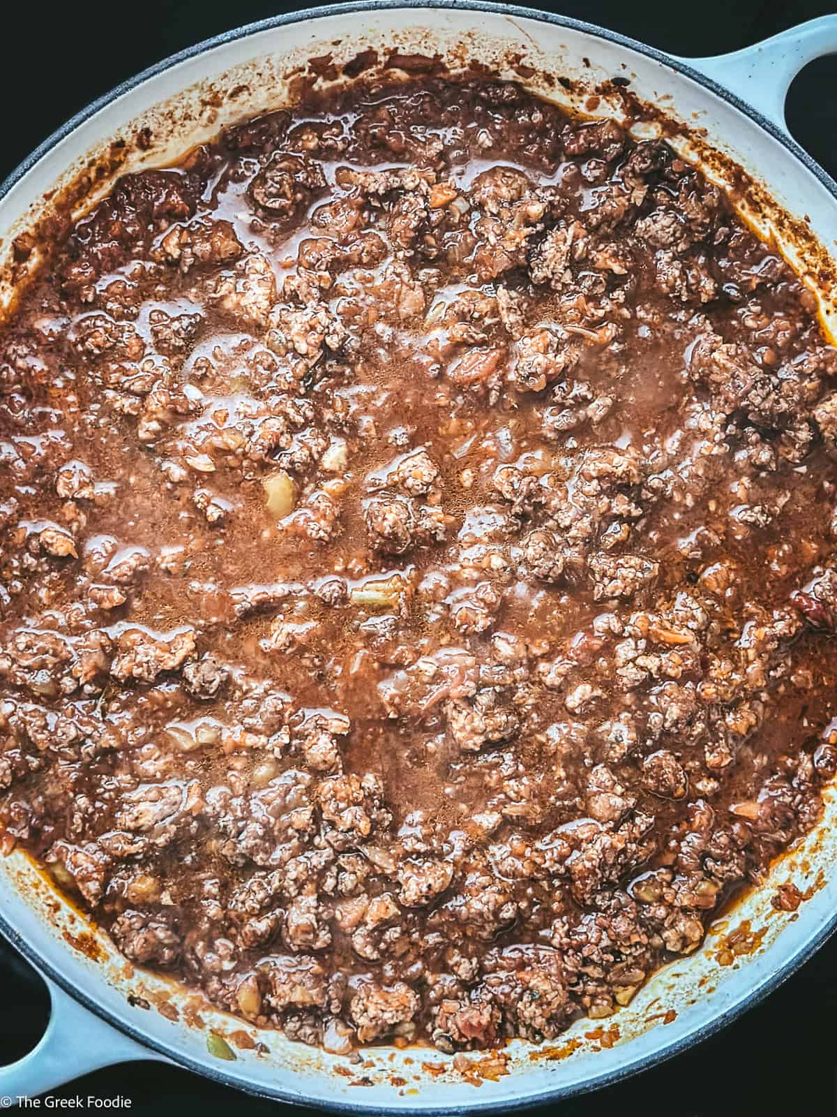 Chicken bolognese in a pot cooking with a sprig of thyme.