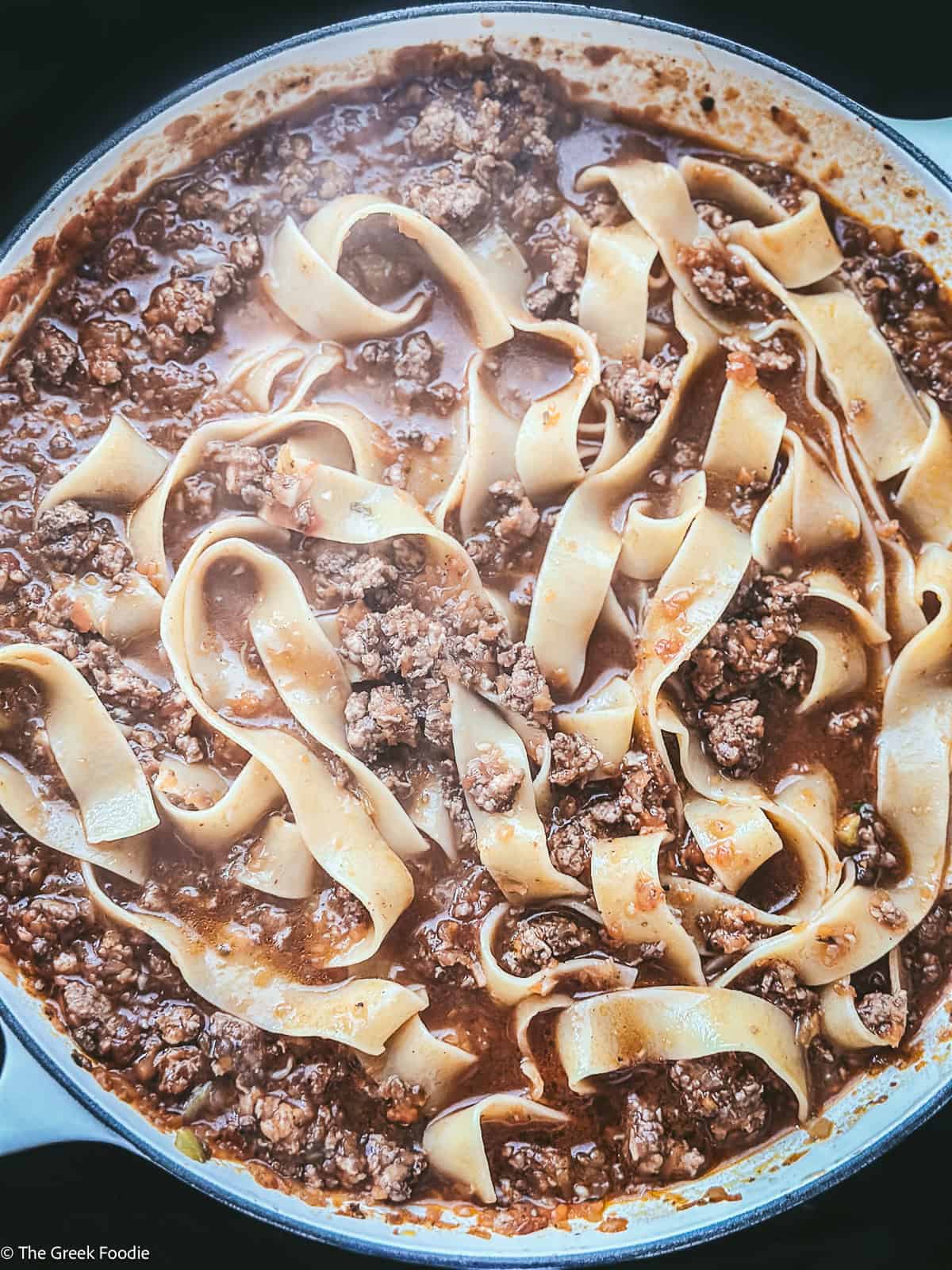 Chicken bolognese with pappardelle pasta in a pot cooking.