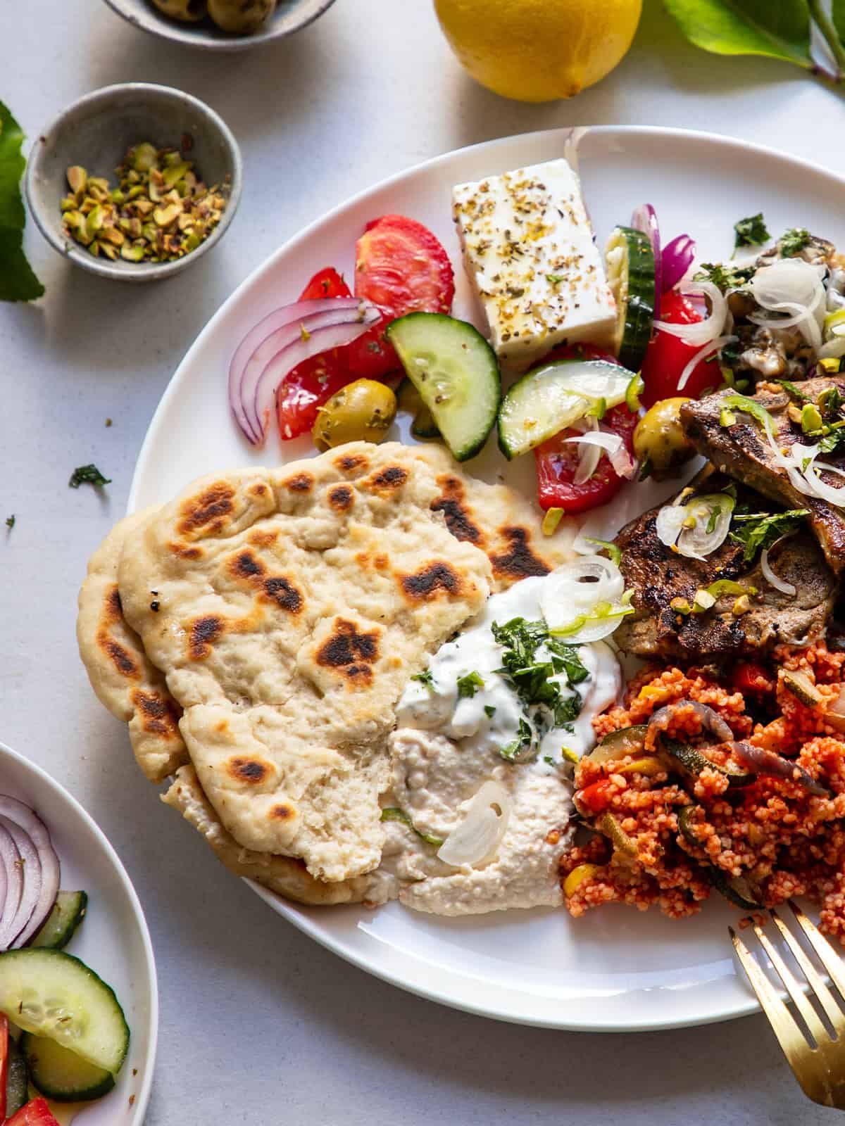 A plate with pitas, tomato salad with feta and dips, and smaller plates on a table.