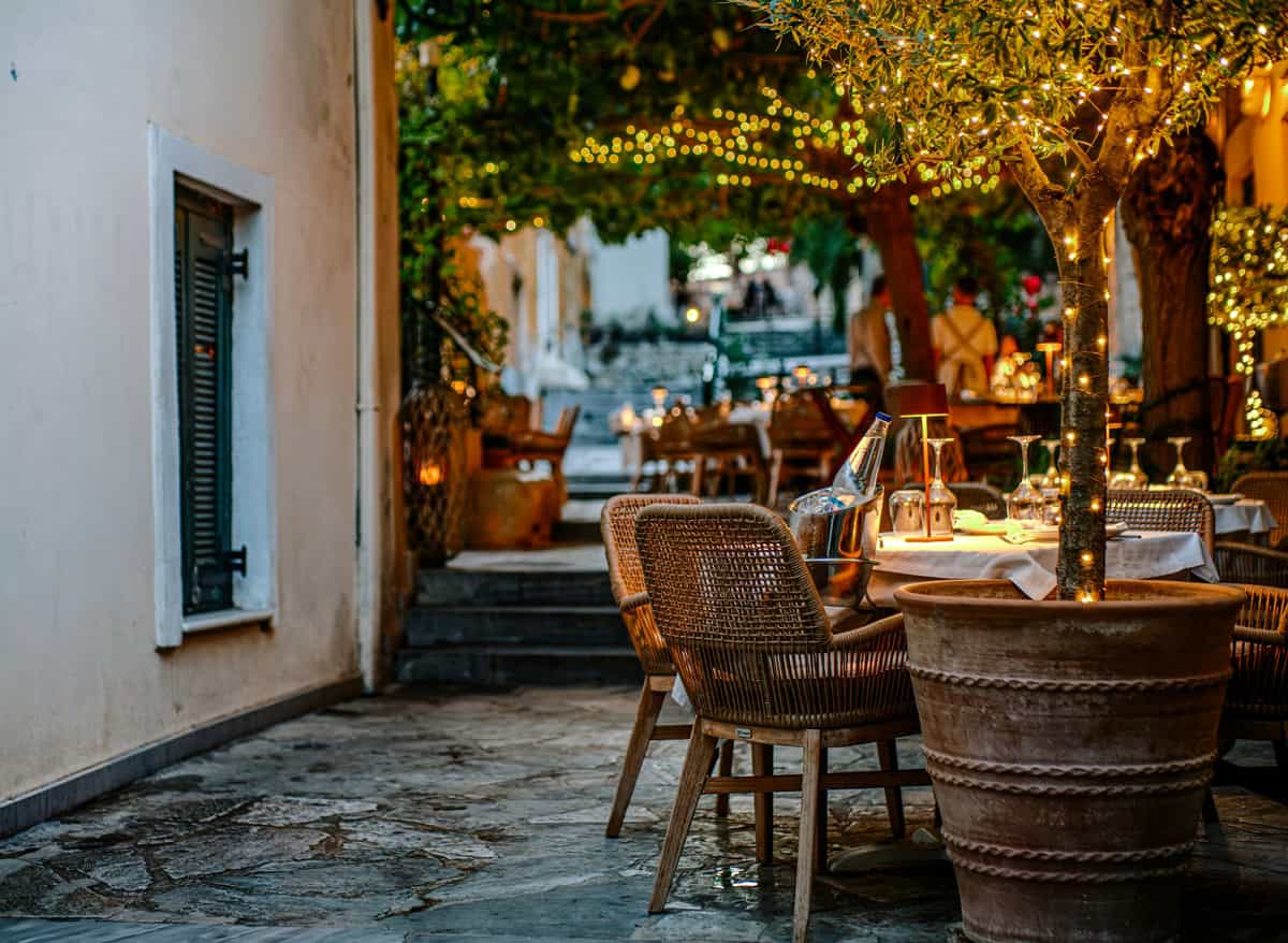 Tables and chairs of a restaurant at a small street in Plaka Athens with small lights.