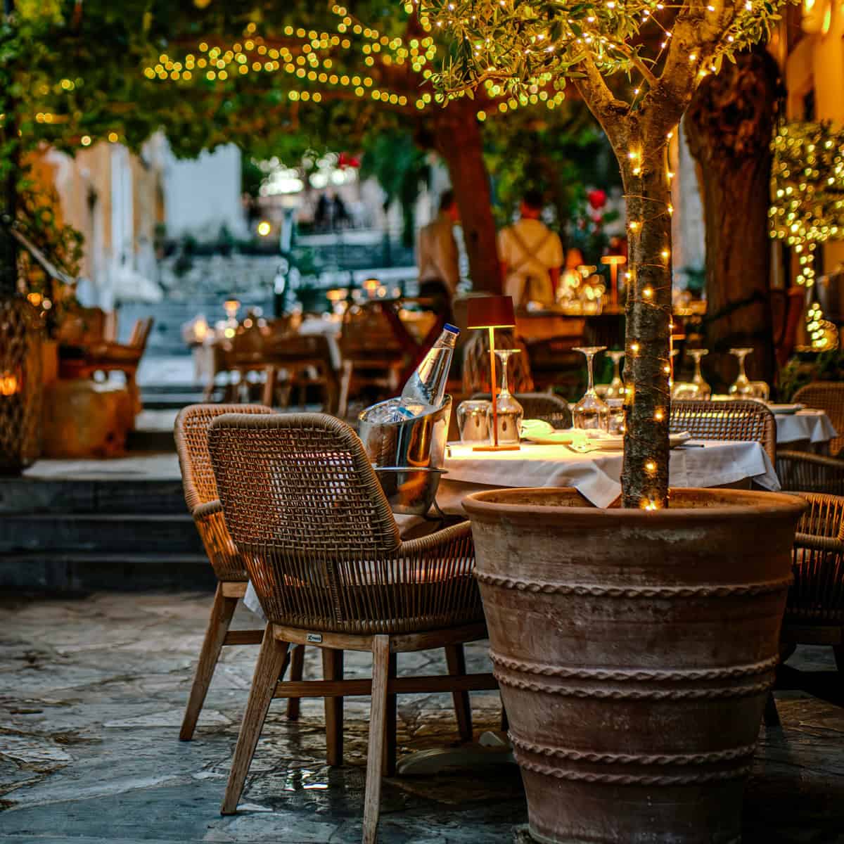 Tables and chairs of a restaurant at a small street in Plaka Athens with small lights.